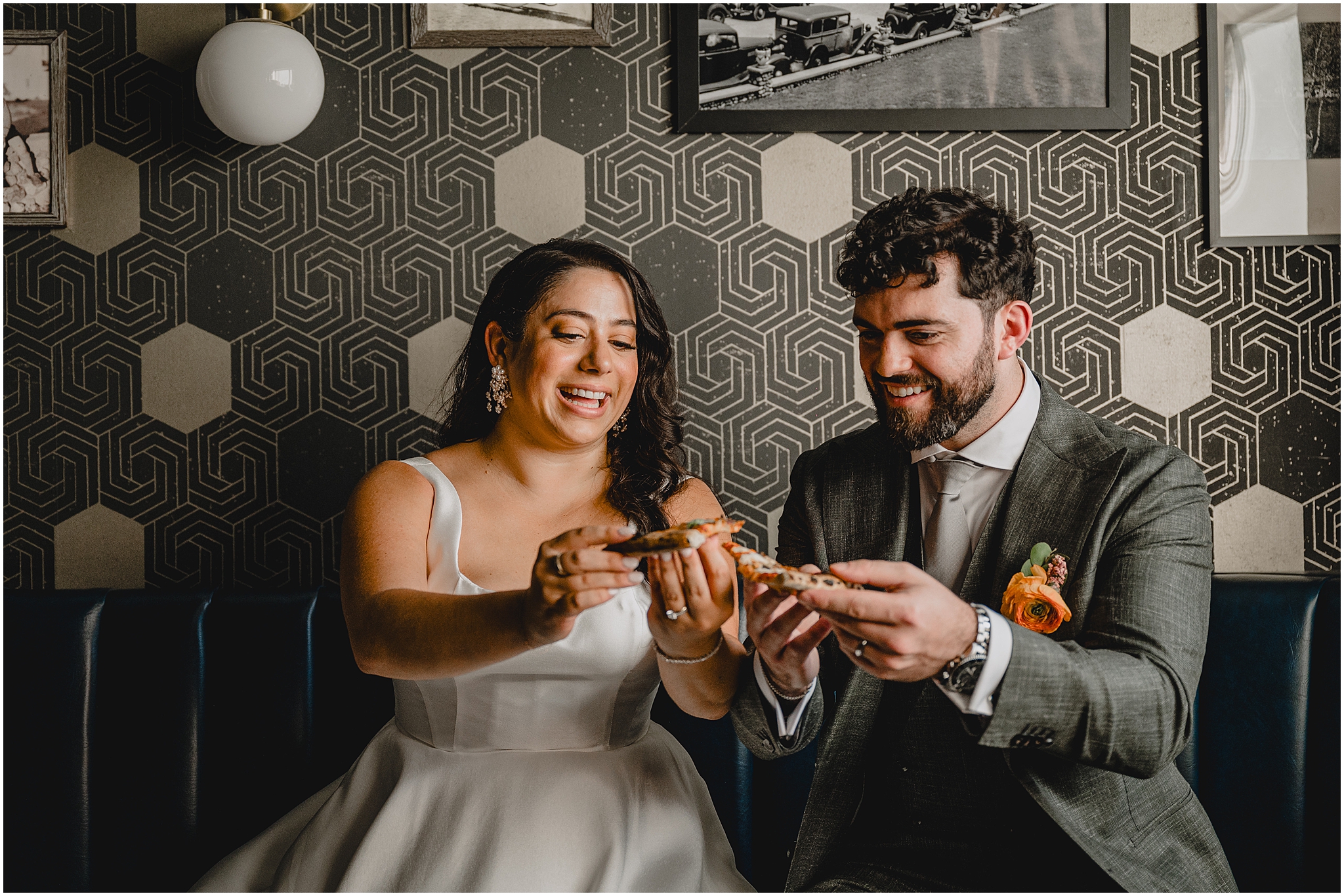 newlyweds laugh toasting slices of pizza in front of black and white wall at the Perona Farms Refinery