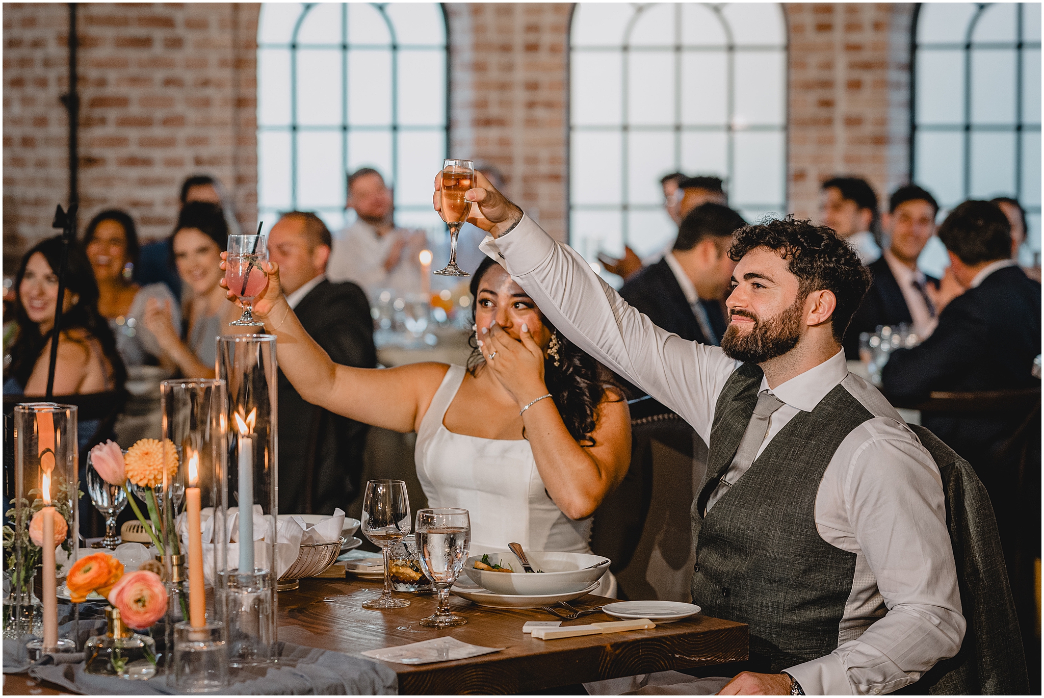 bride and groom lift up glasses sitting at sweetheart table during NJ wedding reception