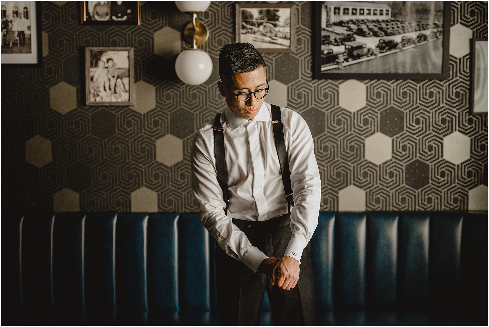 groom adjusts cufflinks of white shirt in front of leather couch and walls with geometric pattern