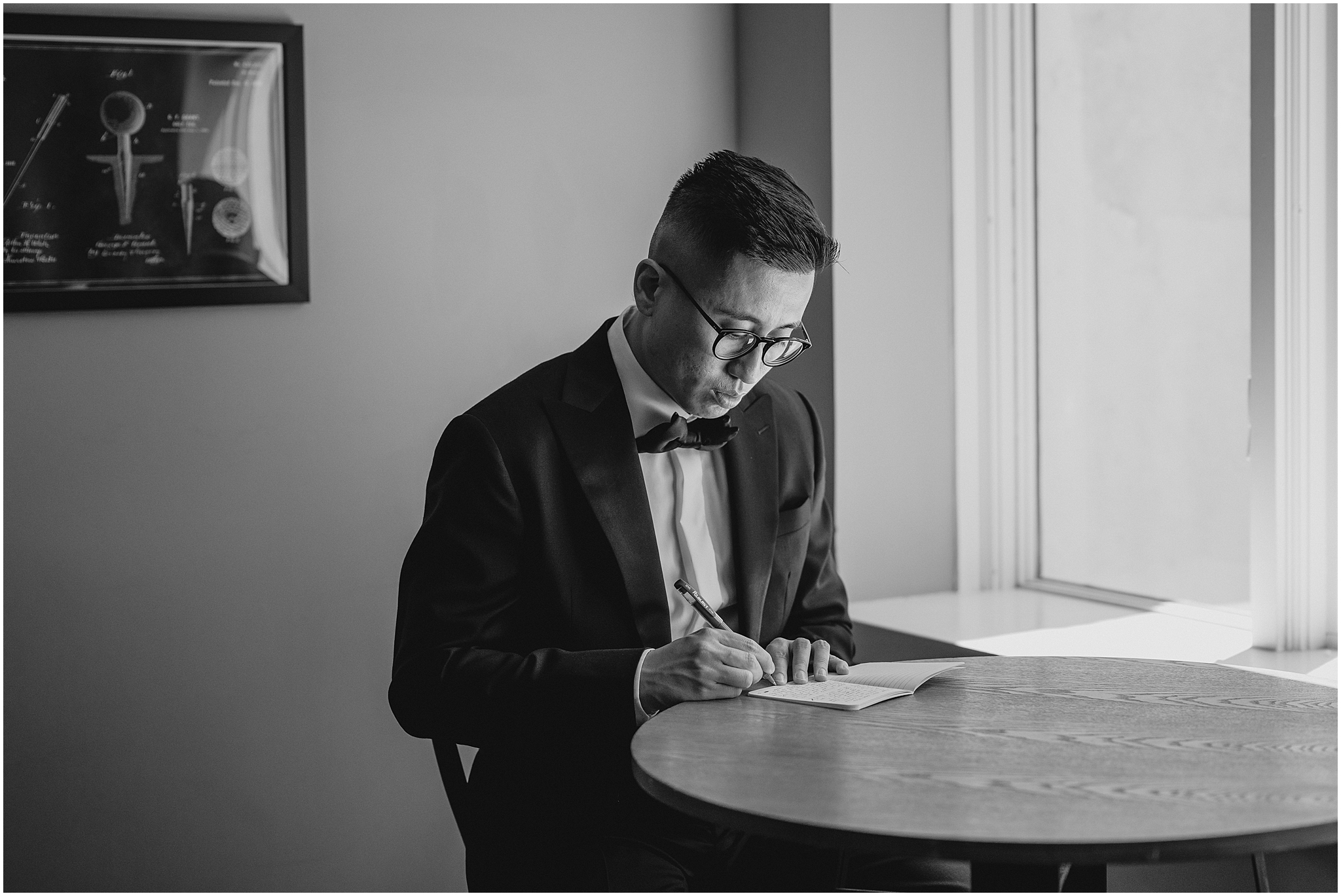 groom writes card to bride at wooden table in suite at the Refinery at Perona Farms