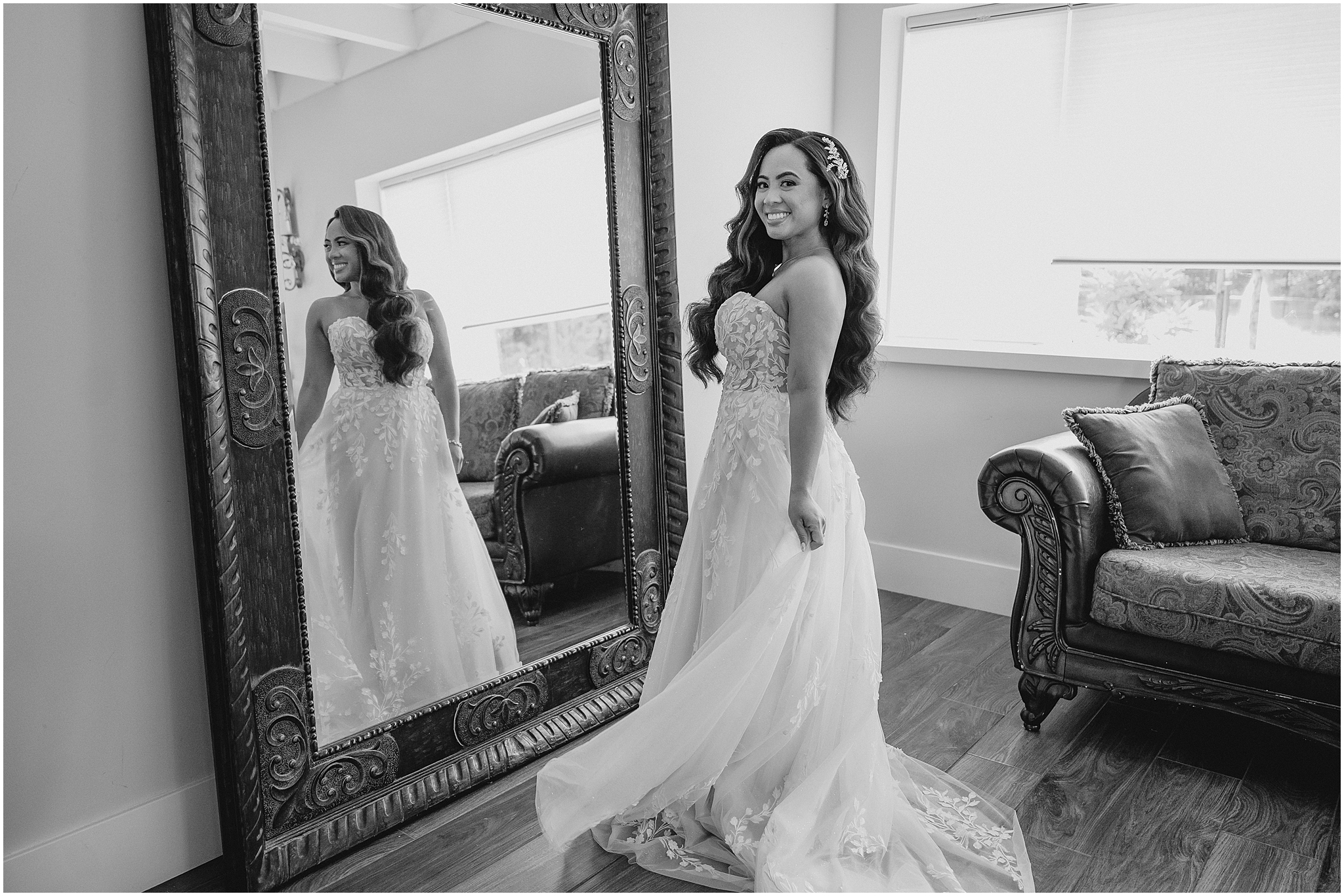 dark haired bride turns in wedding dress holding her skirt by the mirror in bridal suite