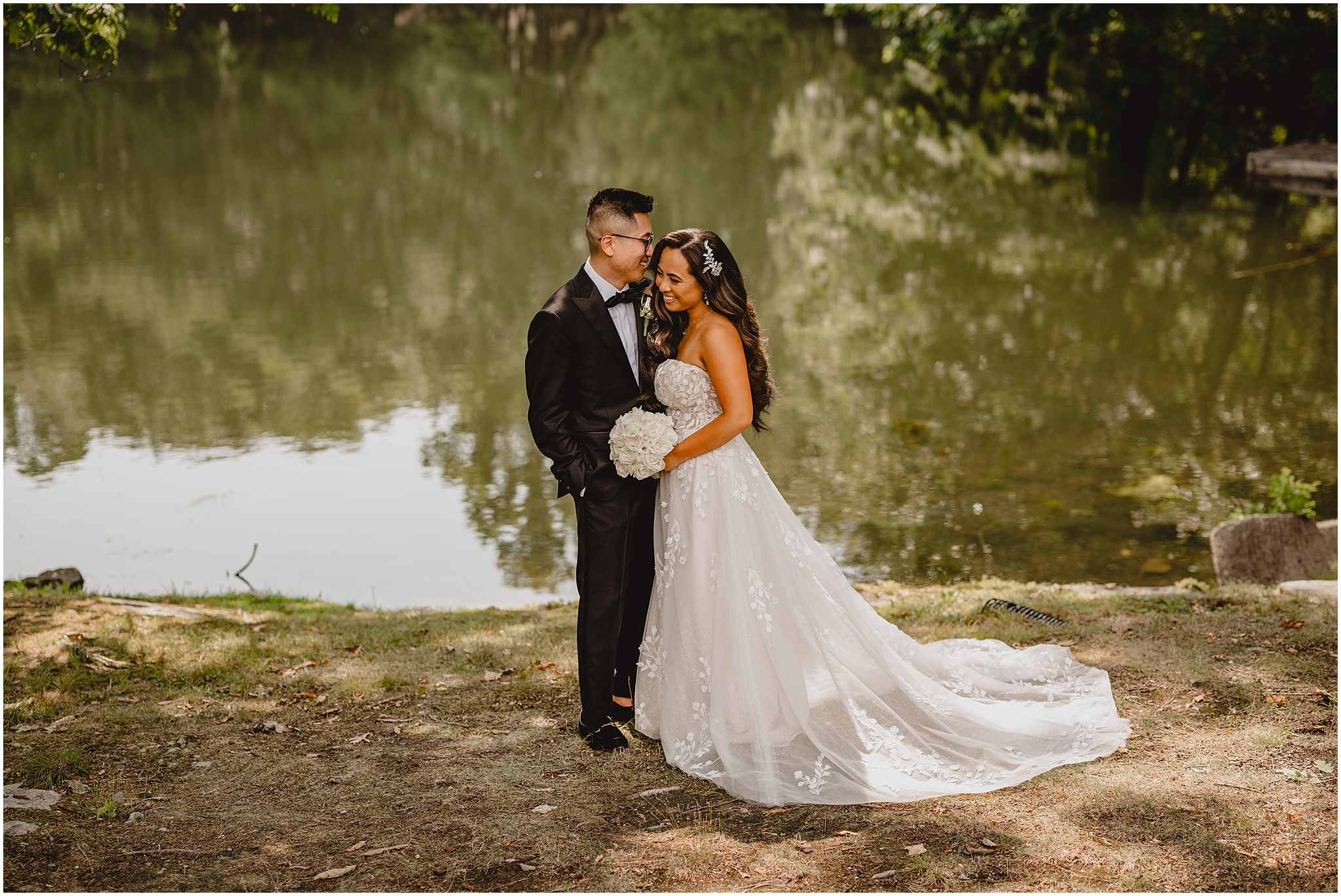 bride and groom laugh by pond during wedding portraits at the Refinery at Perona Farms