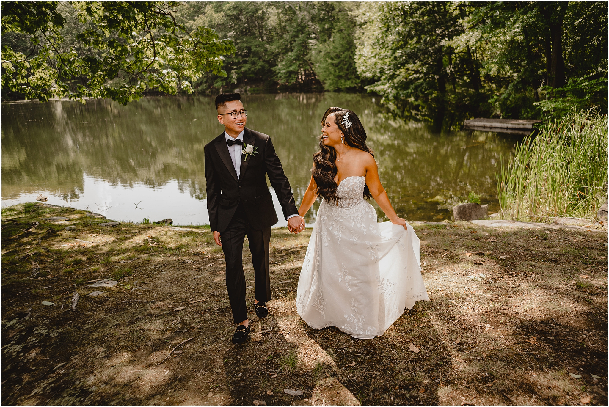 bride and groom hold hands walking away from pond in Andover NJ