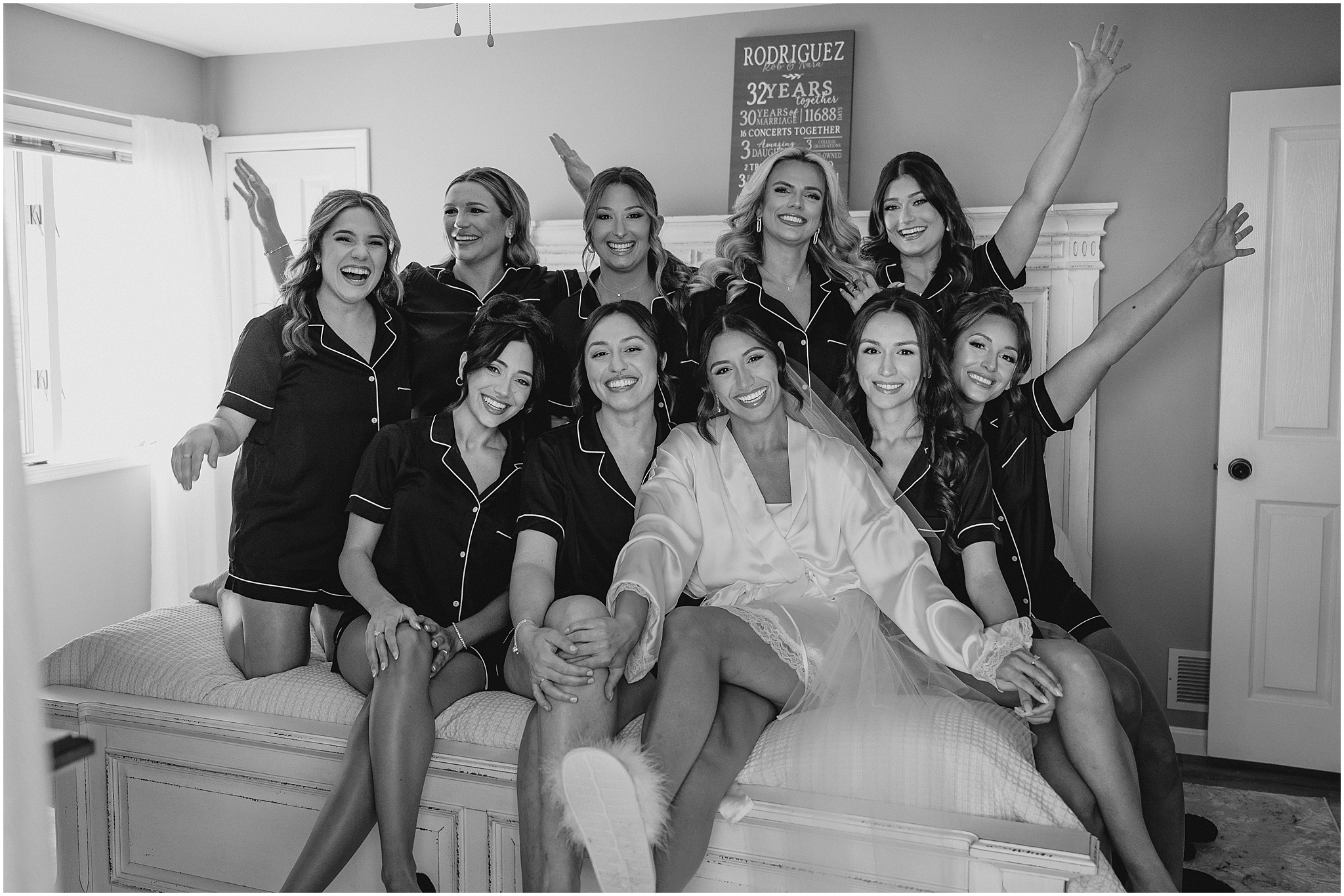 bride grins with bridesmaids around her cheering on bed in NJ hotel