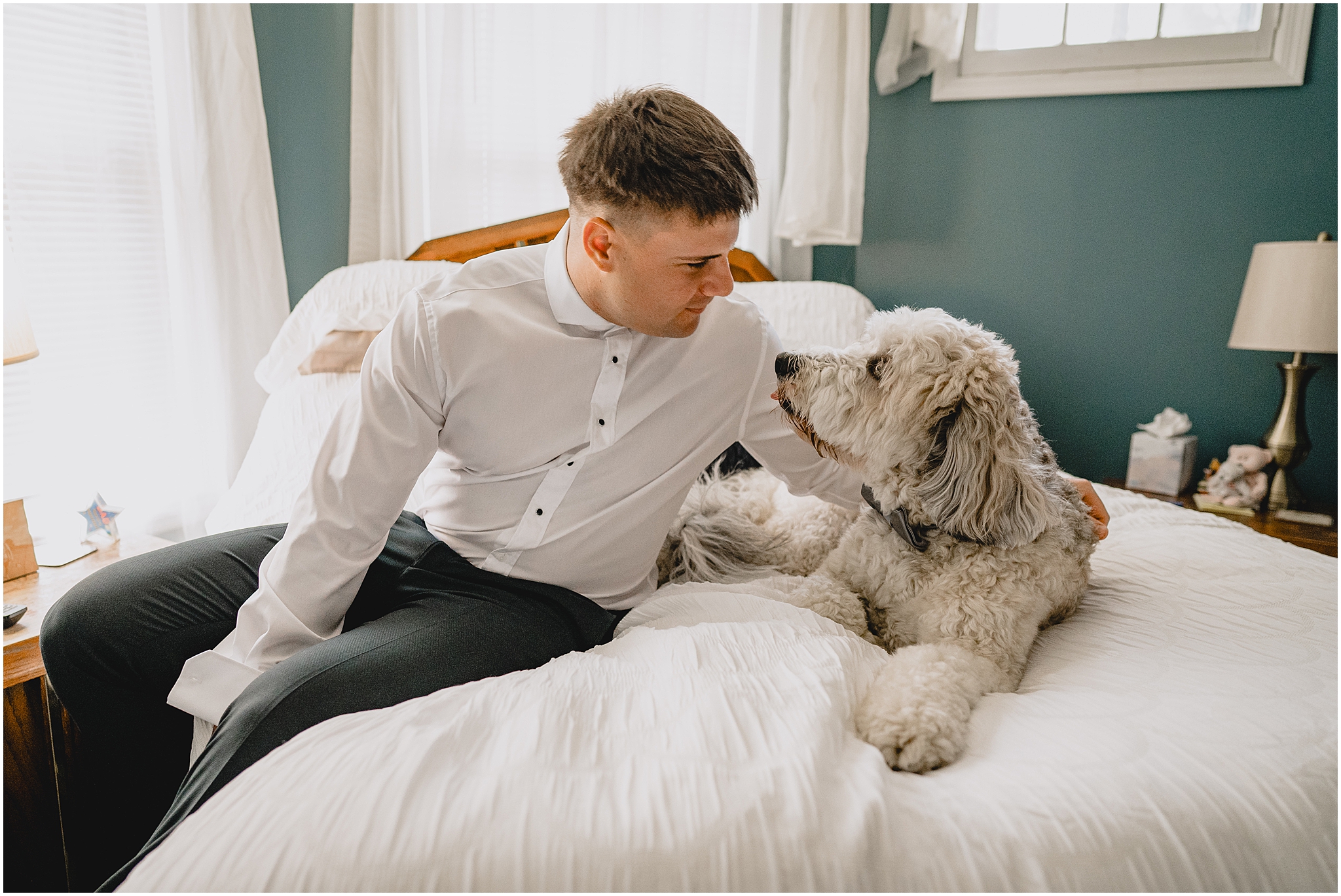 groom sits on bed looking at dog before NJ wedding day