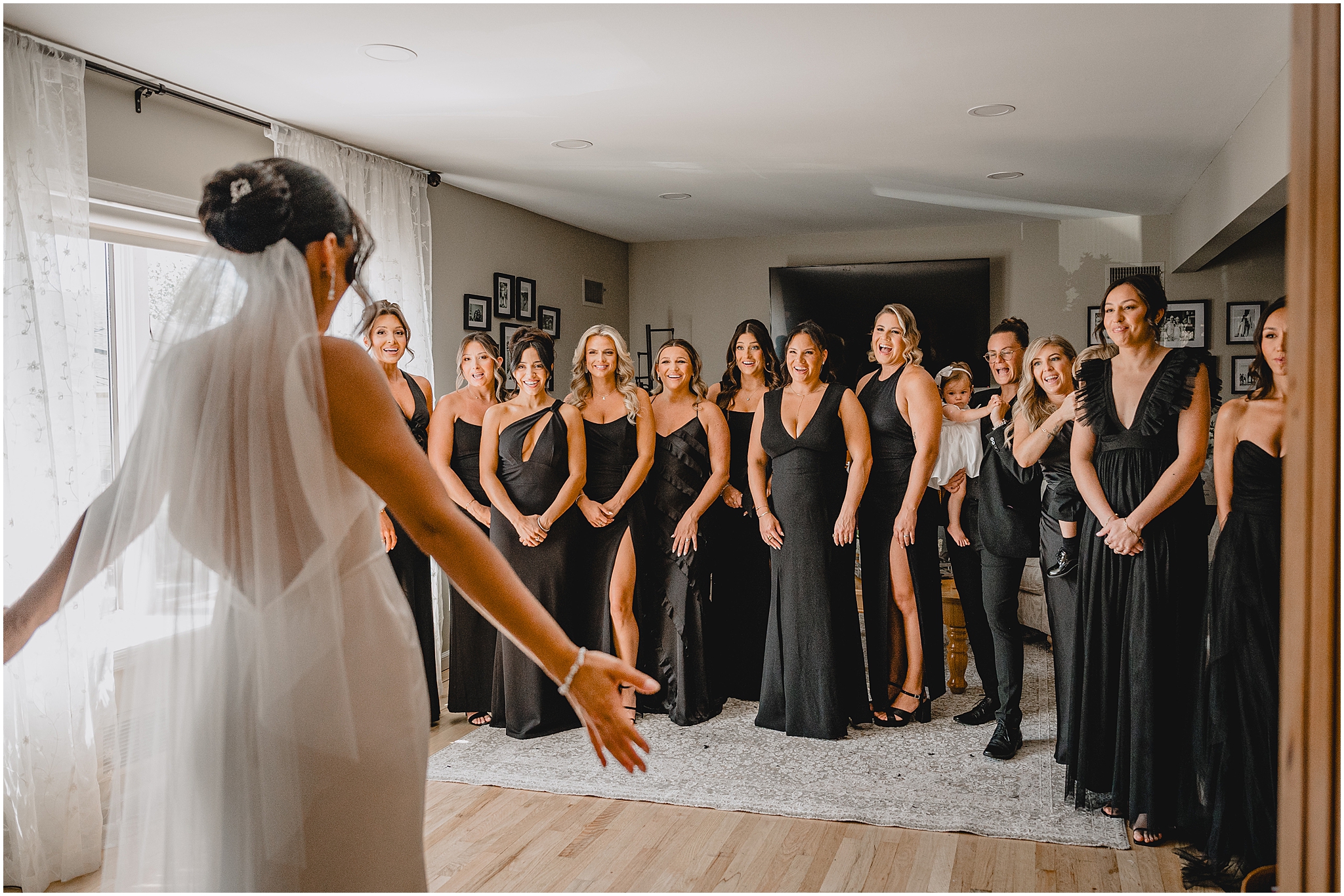 bride shows off wedding dress to bridesmaids in black dresses during first look 