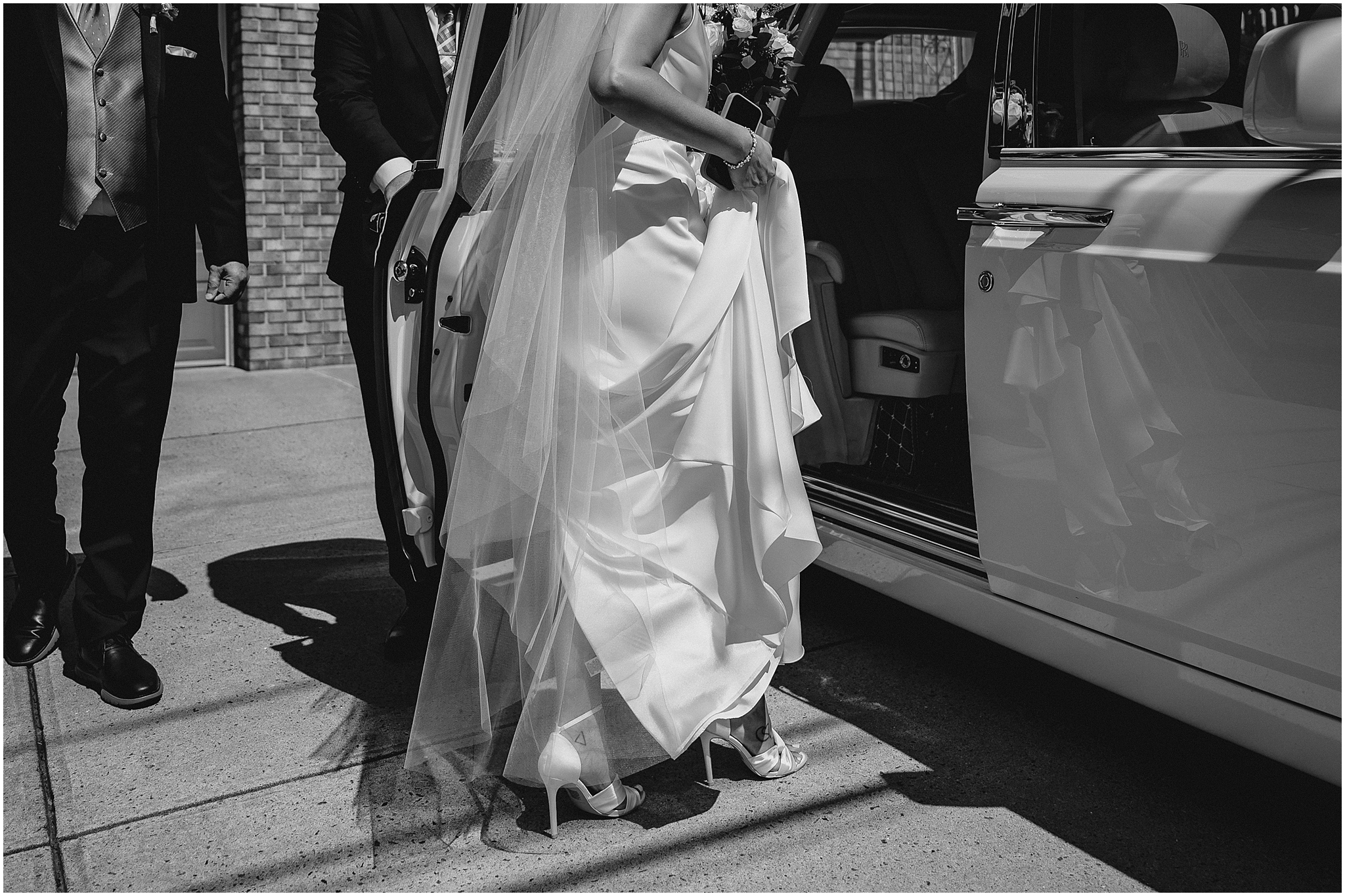 bride lifts up dress to step into white car on wedding day