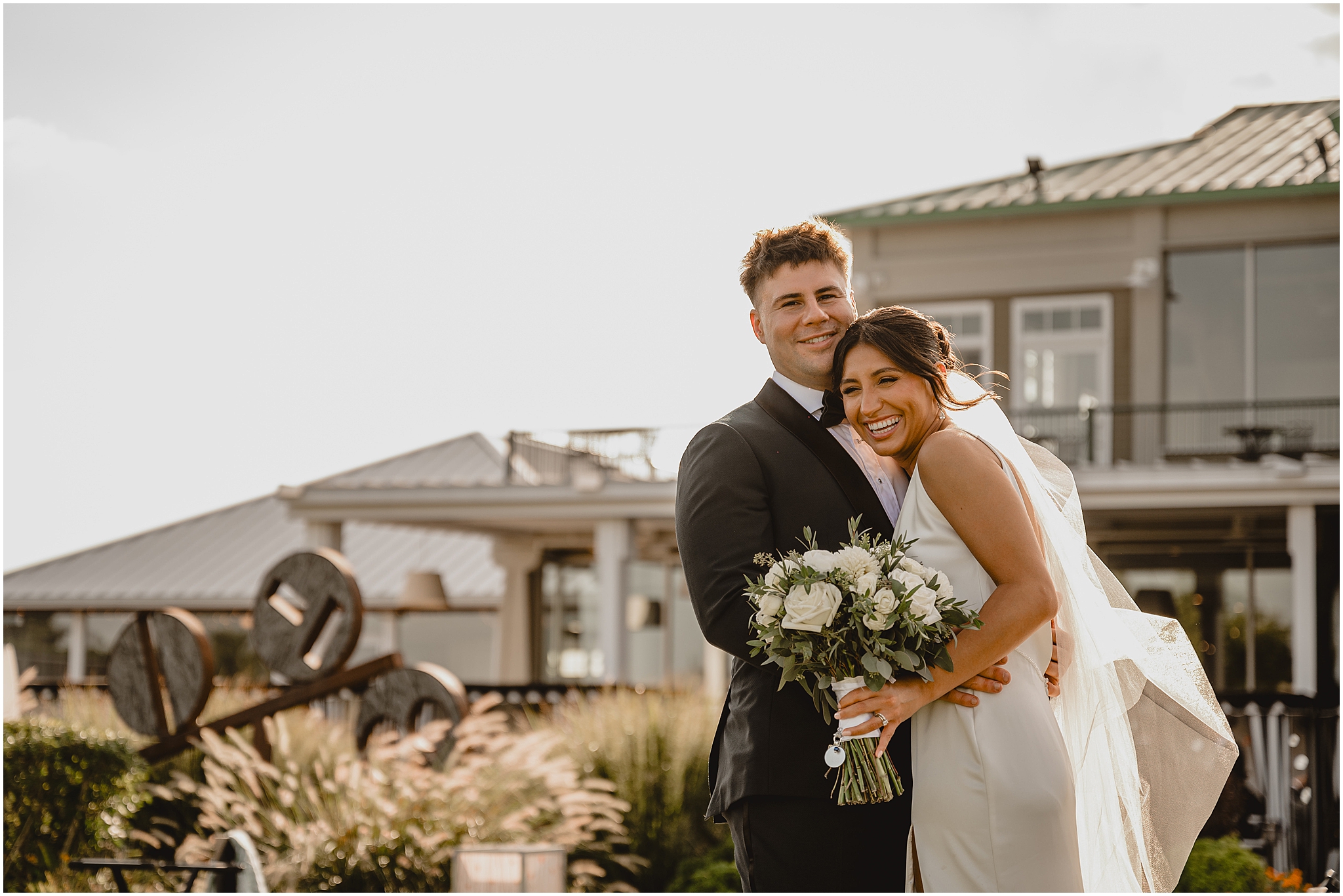 bride laughs leaning into groom standing in front of the Liberty House in Jersey City