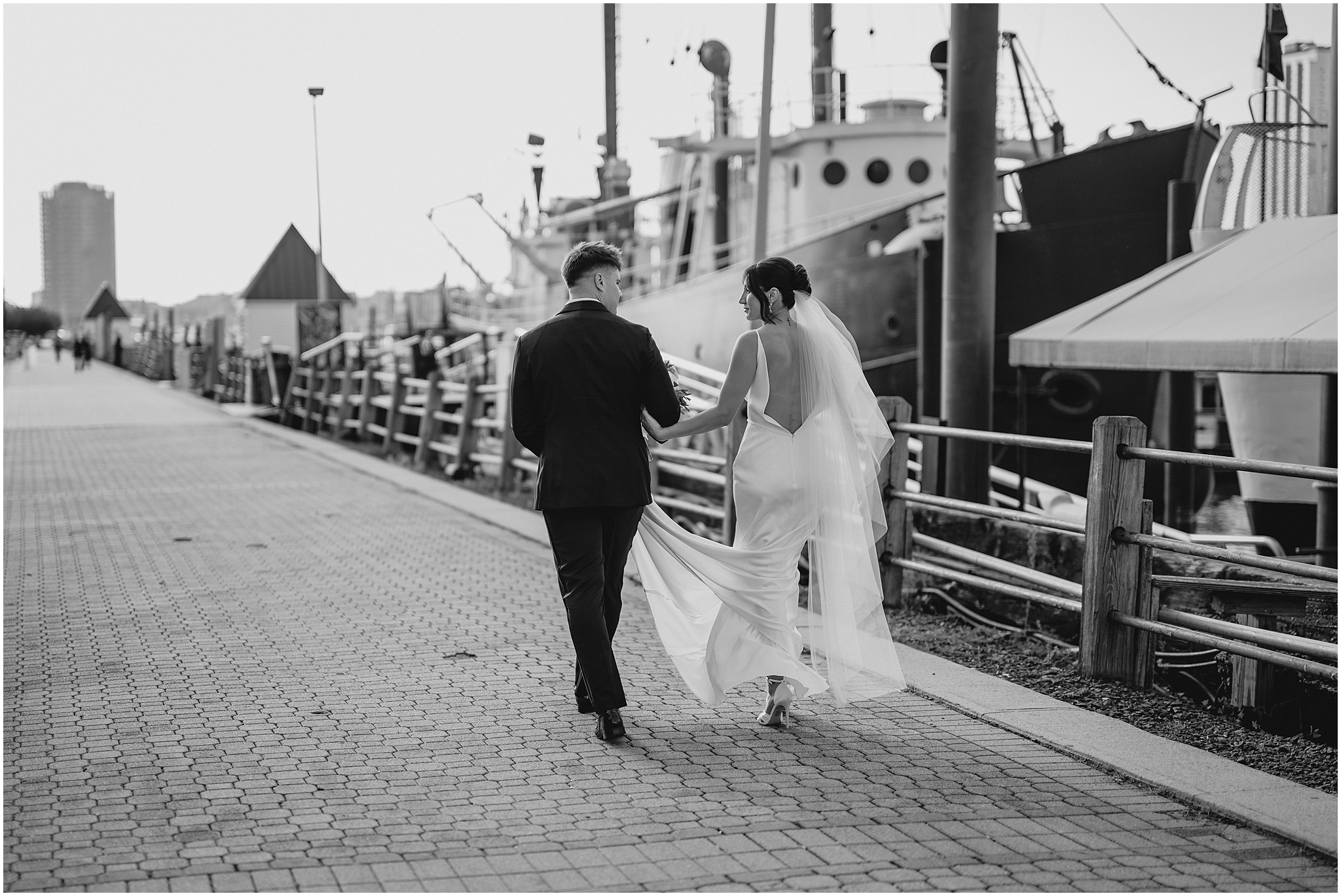 bride and groom hold hands walking down marina outside the Liberty House in Jersey City