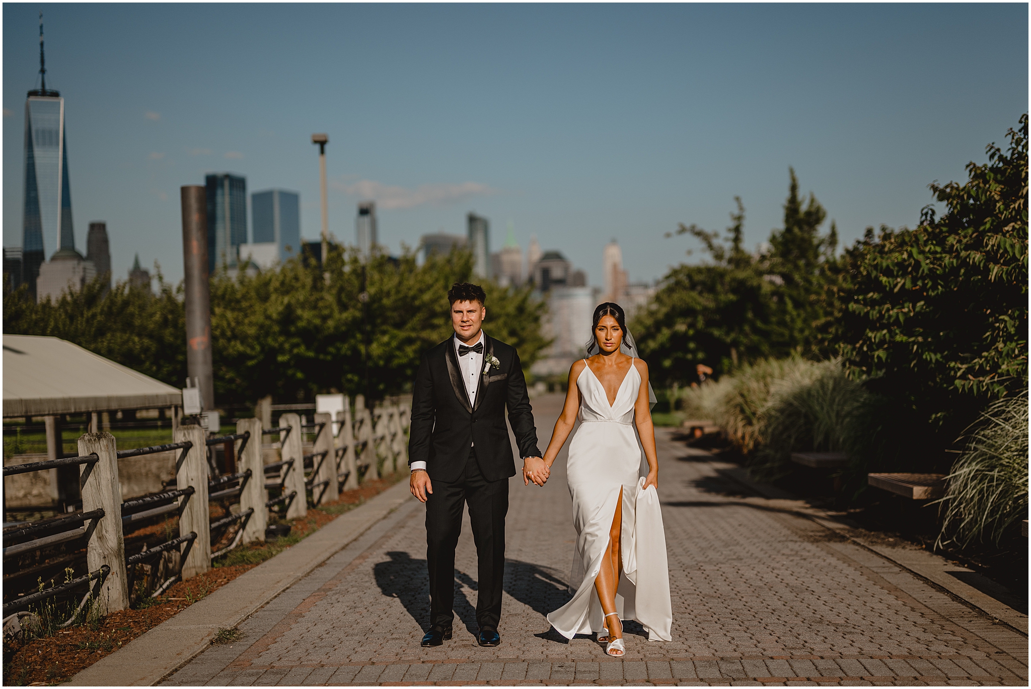 bride and groom stand on walkway with Manhattan skyline behind them