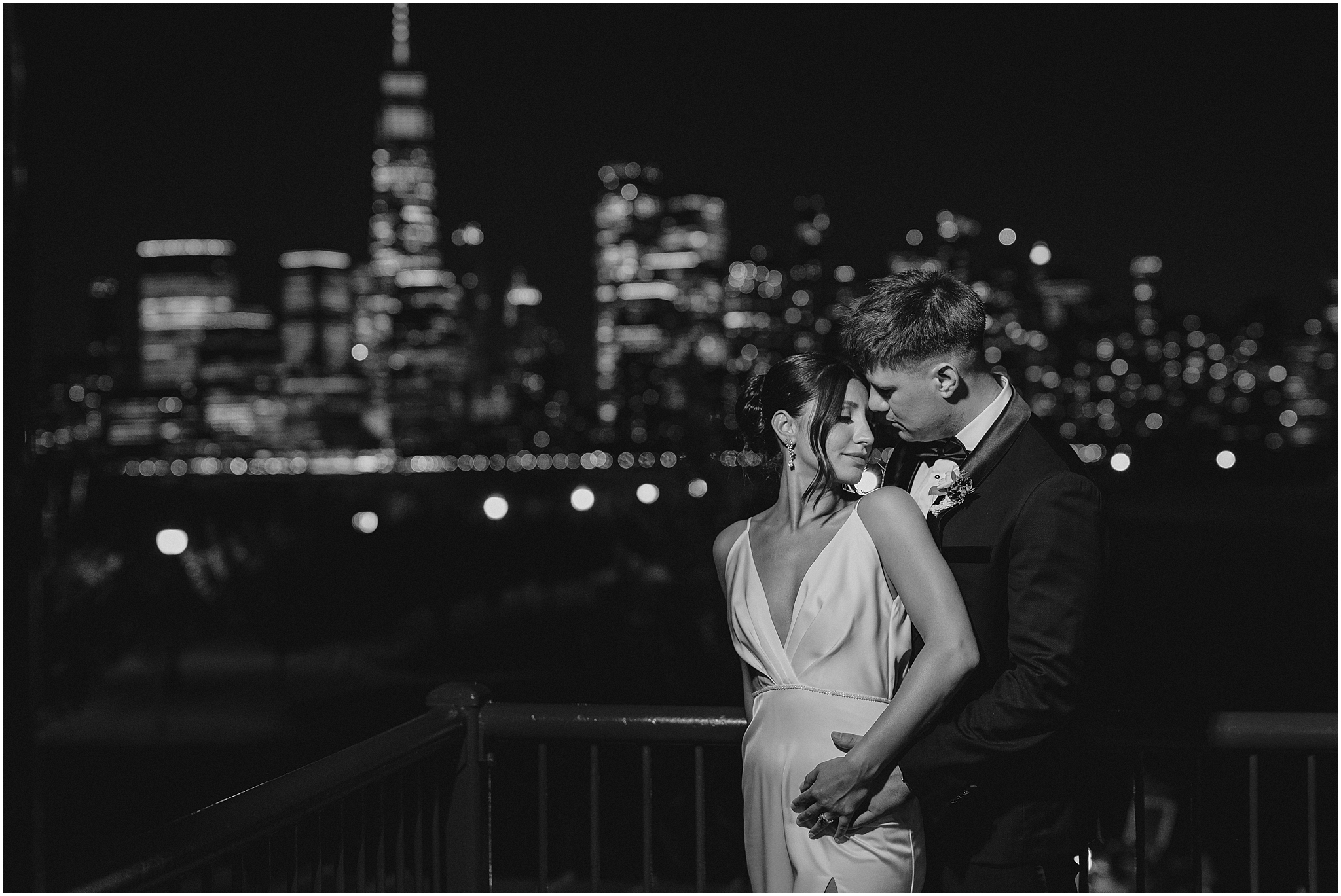 bride and groom hug on balcony with NYC skyline behind them at night 