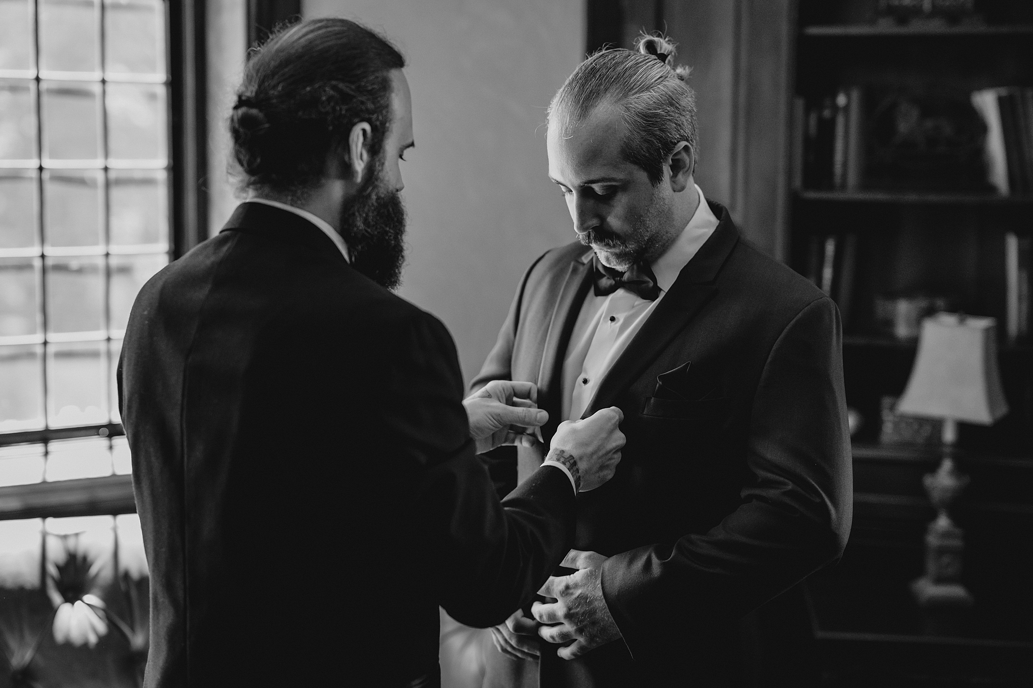 groomsman help groom with suit jacket inside library at Pleasantdale Chateau