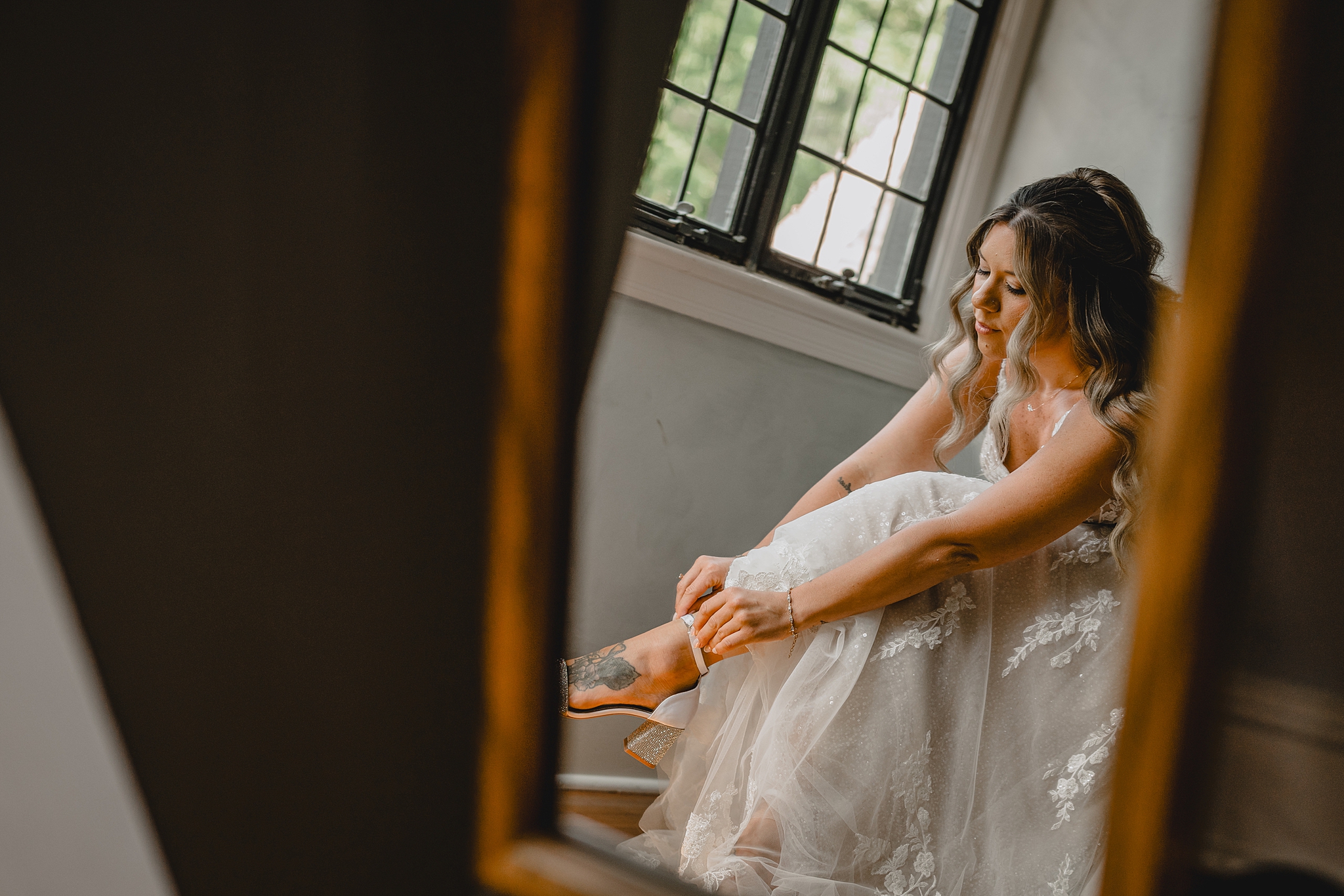 bride adjusts strap of ivory shoes in mirror reflection at Pleasantdale Chateau