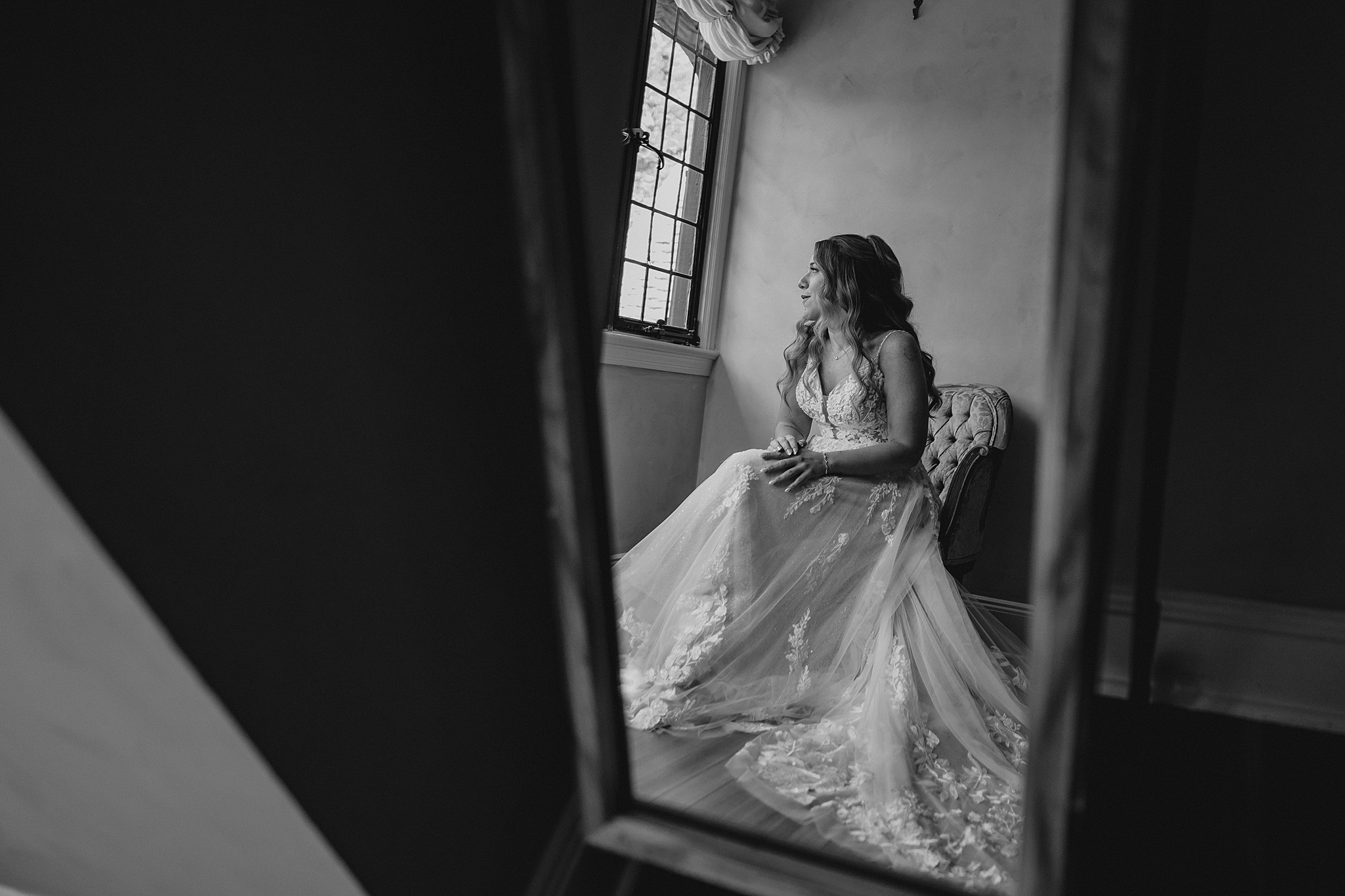 reflection of bride sitting in plush chair looking out the window at Pleasantdale Chateau
