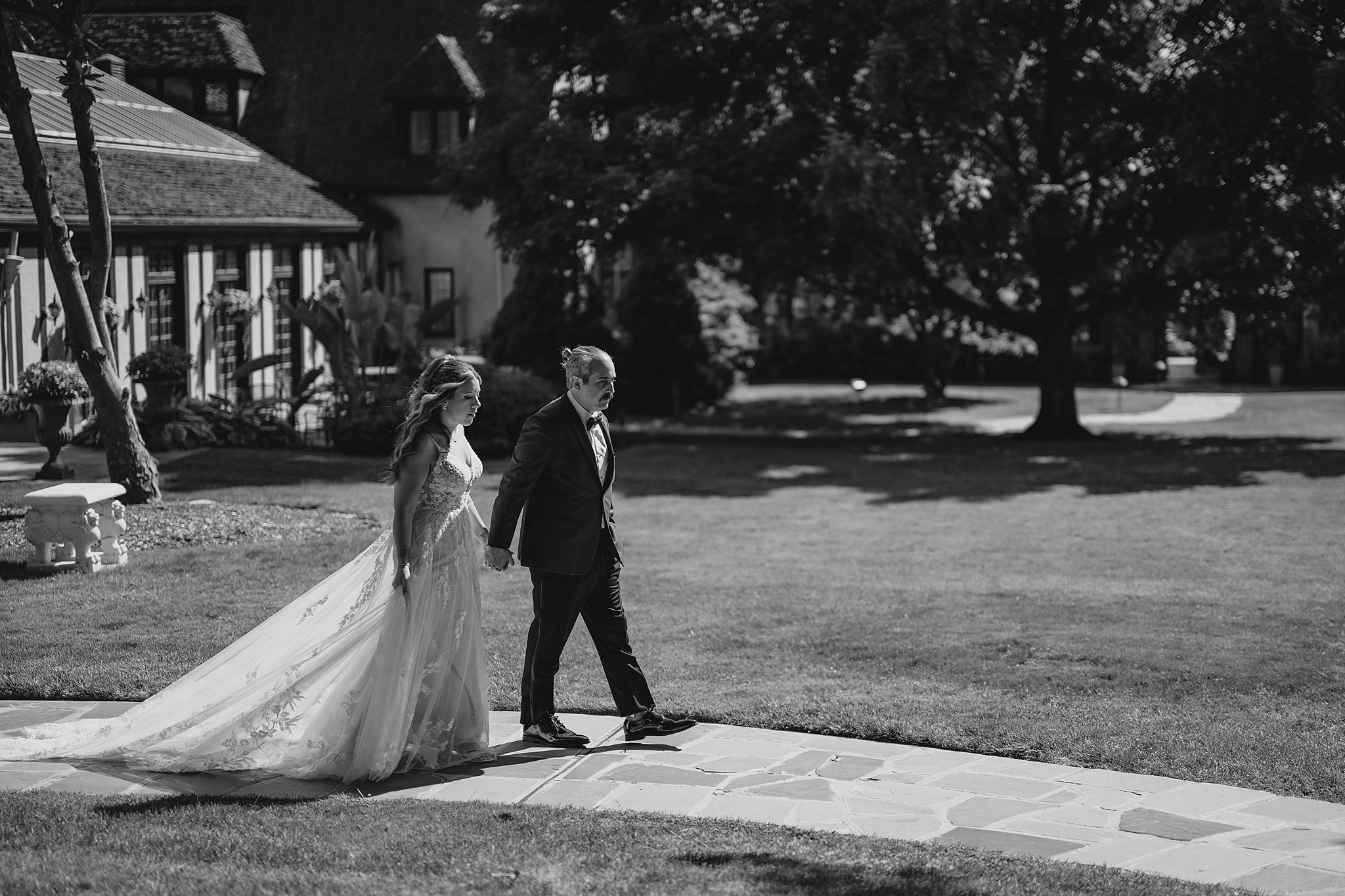 newlyweds hold hands walking on pathway during summertime wedding portraits 