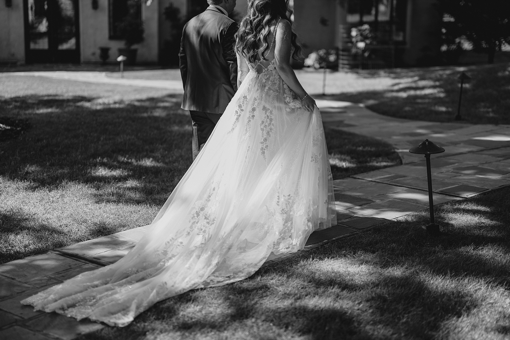 newlyweds hold hands walking down pathway outside Pleasantdale Chateau