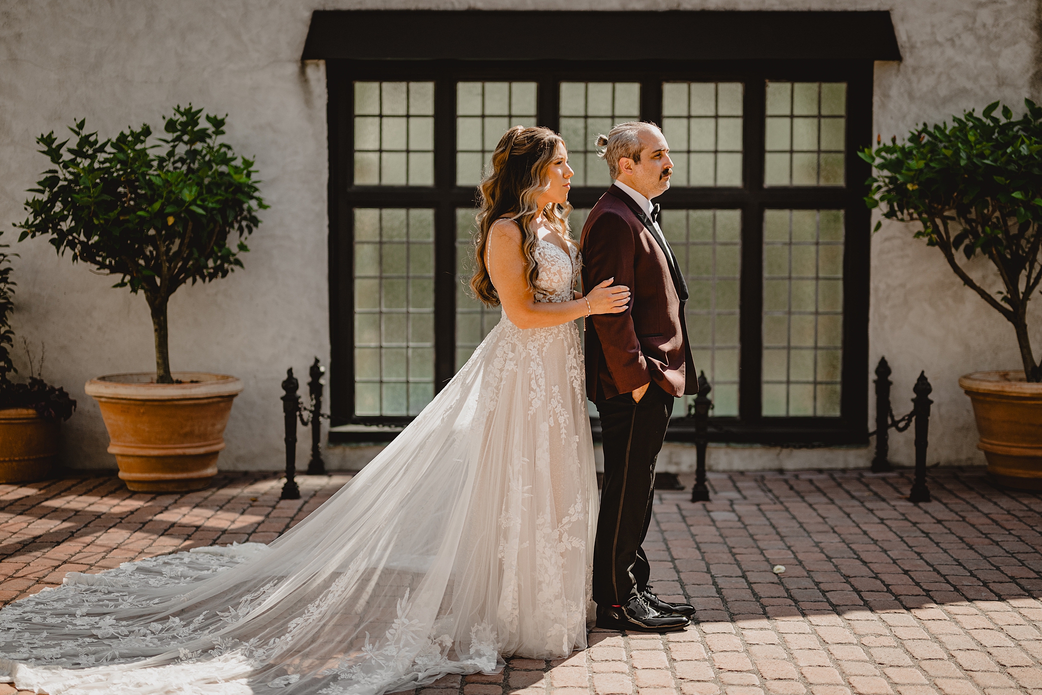 bride stands behind groom in burgundy suit jacket during West Orange NJ wedding photos