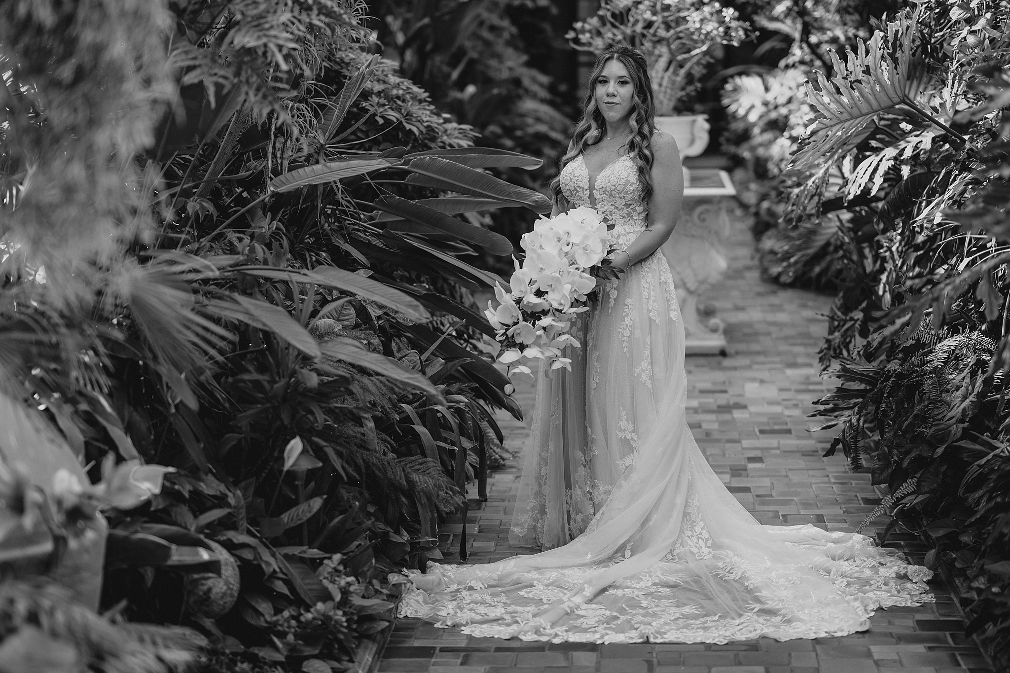 bride stands on brick patio holding cascading bouquet of white flowers in gardens at Pleasantdale Chateau
