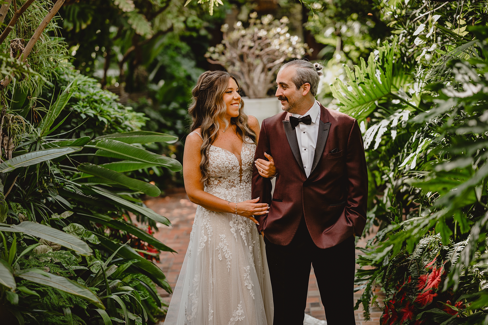bride holds groom's arm looking at each other in gardens of Pleasantdale Chateau