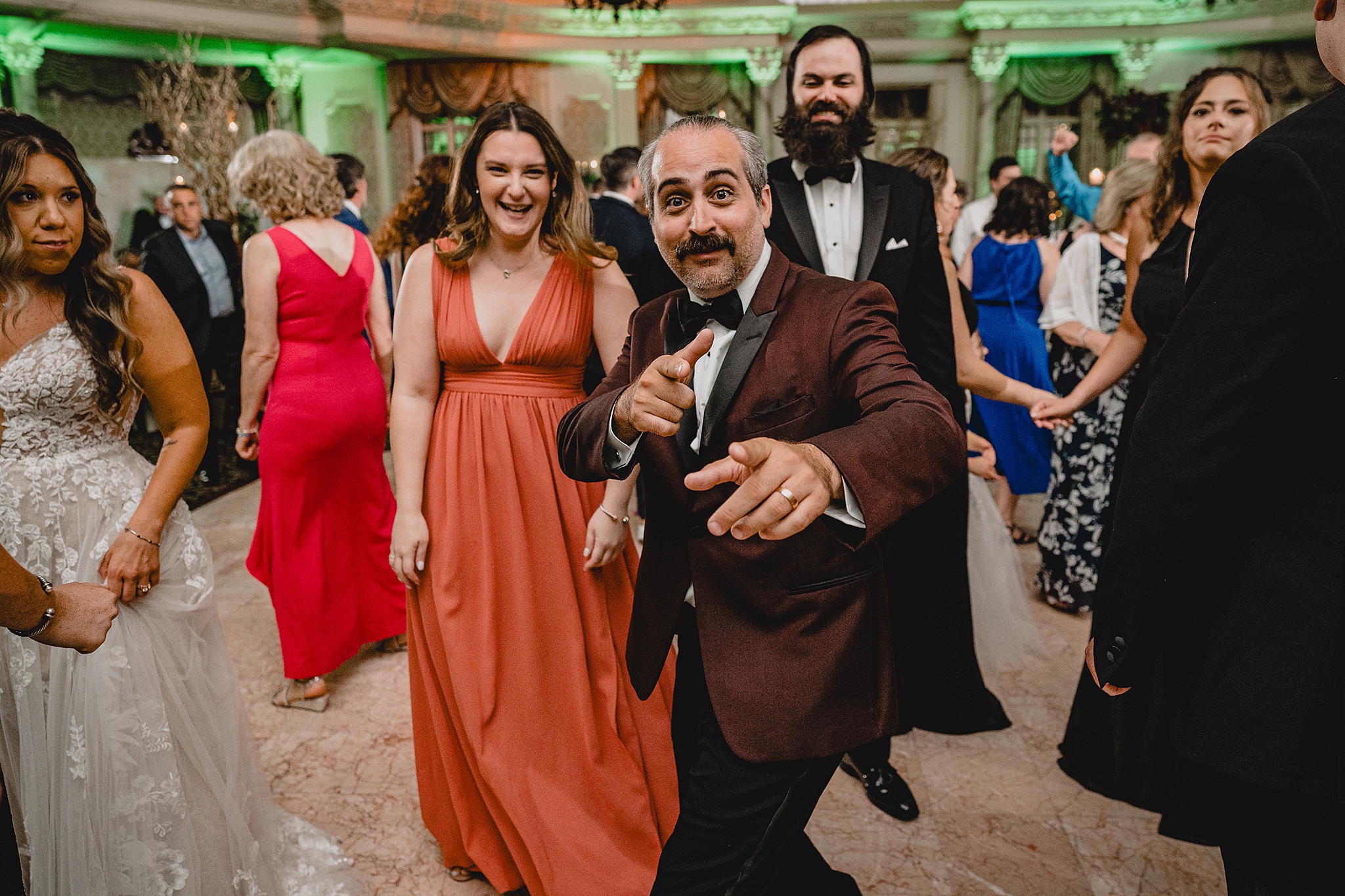 groom grins in red and black jacket inside ballroom at Pleasantdale Chateau