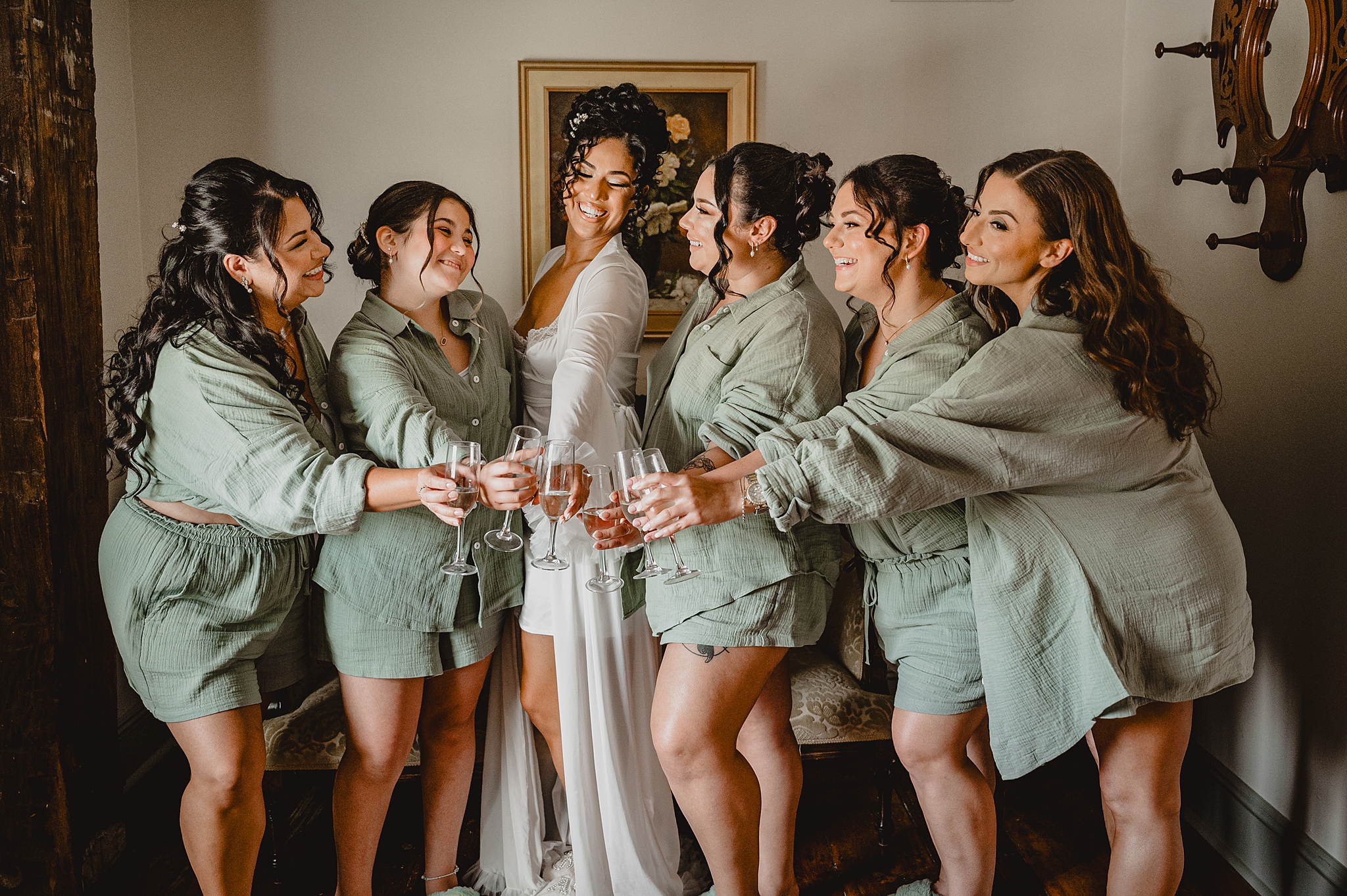 bride toasts champagne with bridesmaids in matching linen sage green pajamas 
