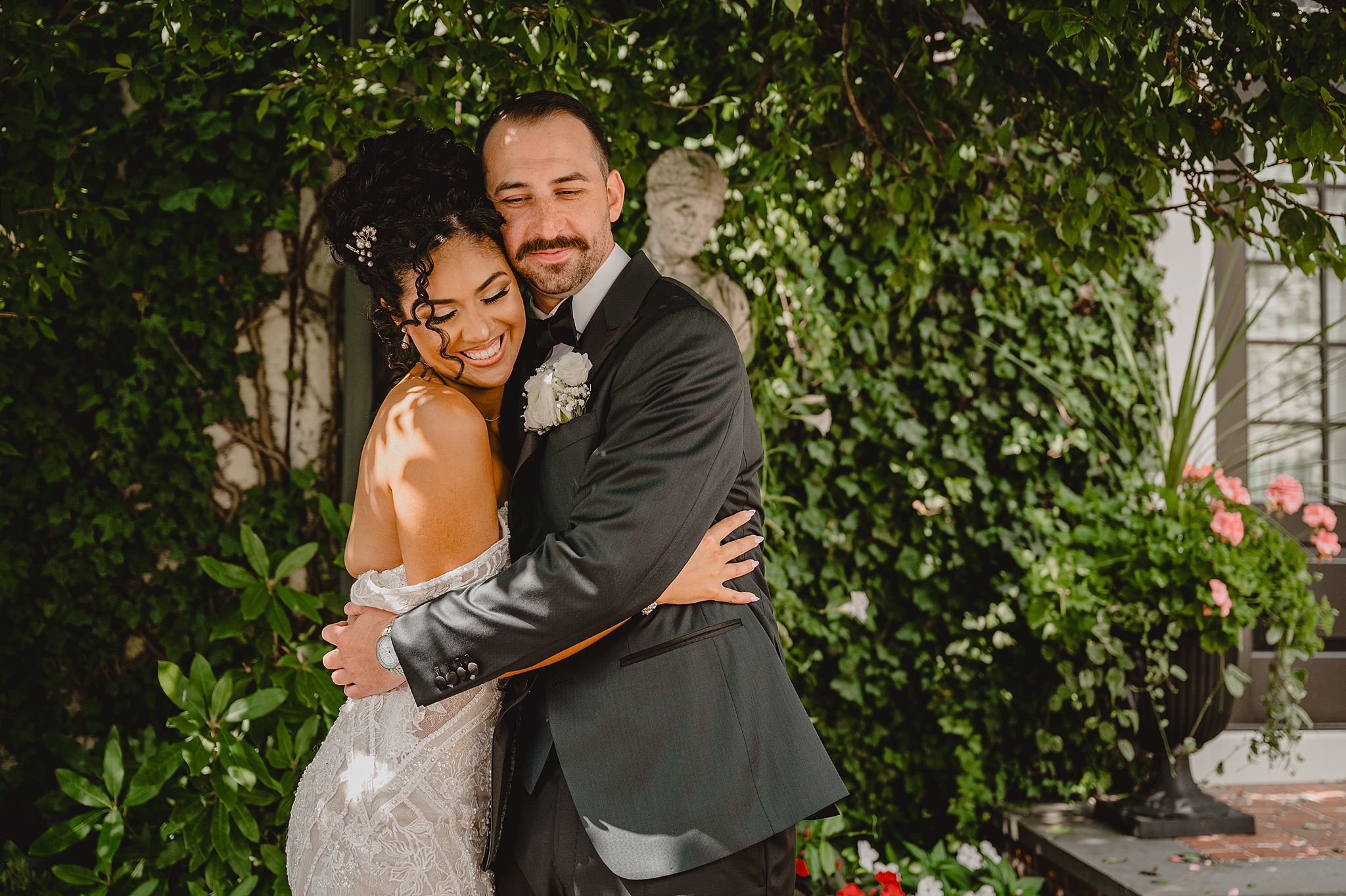 newlyweds hug in front of greenery covered wall at David's Country Inn