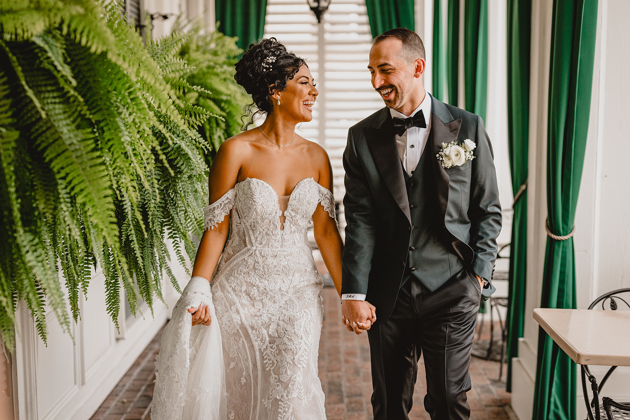 newlyweds hold hands walking by ferns on patio at David's Country Inn