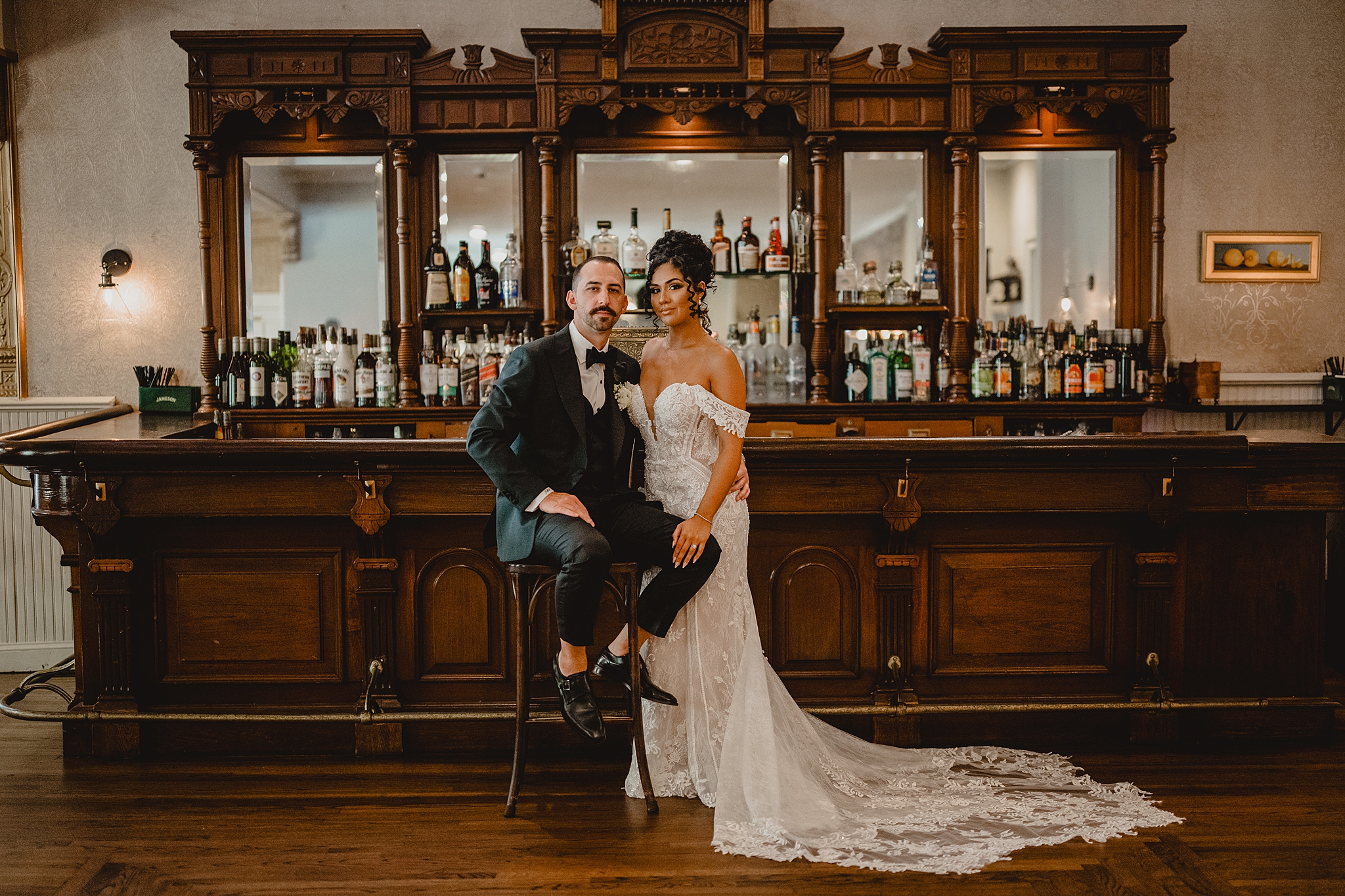 groom sits on barstool with bride standing next to him inside David's Country Inn