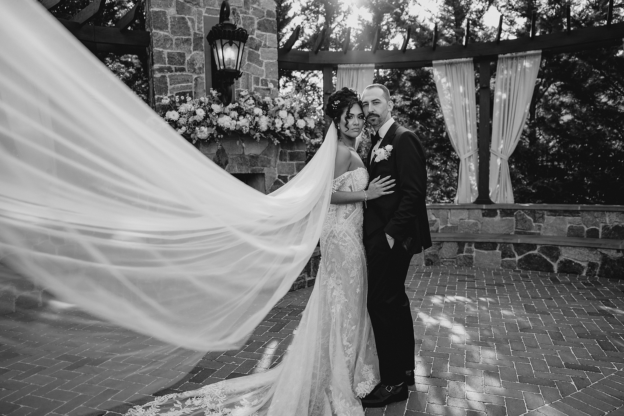 black and white portrait of bride and groom on stone patio with bride's veil pulled out in front of them