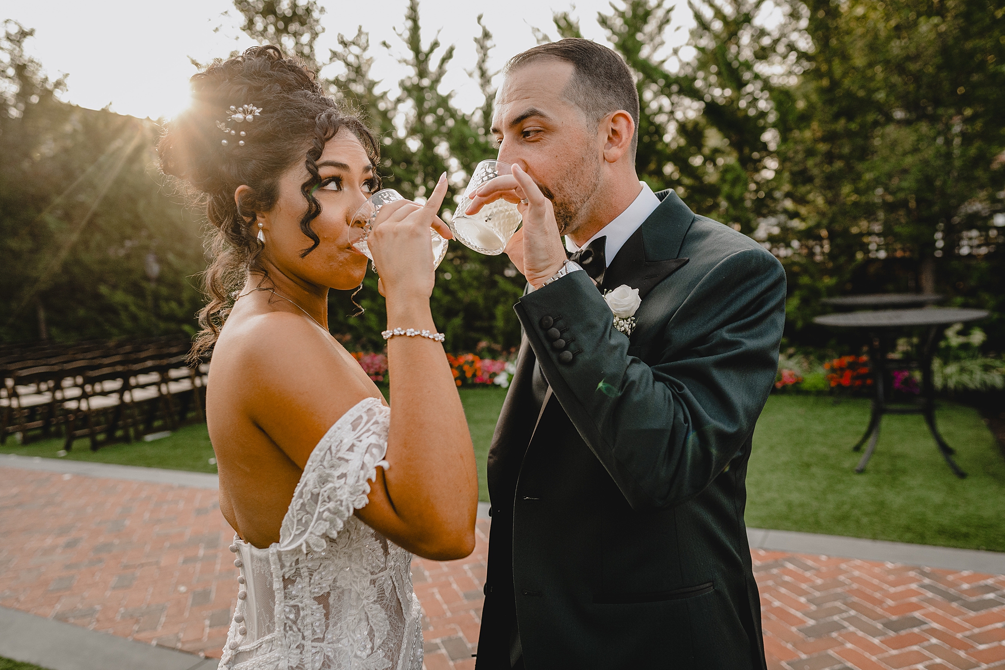 newlyweds smile at each other while drinking cocktails and holding their pinkies up 
