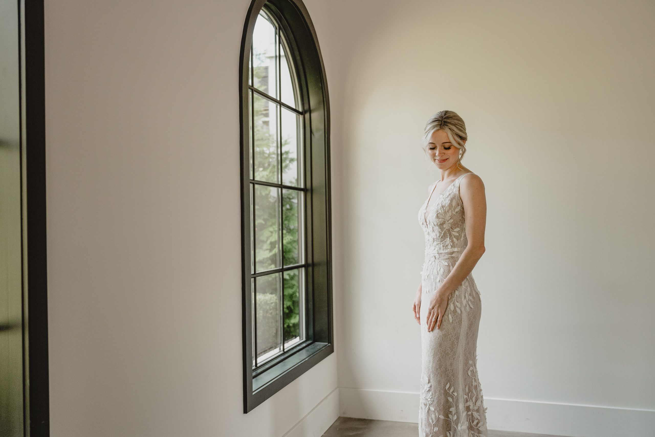 bride stands in wedding gown in front of window at the Perona Farms Refinery
