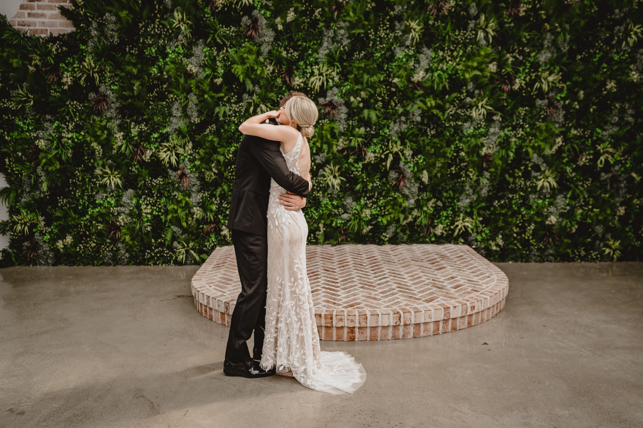 bride and groom hug tight in front of greenery covered brick wall at the Perona Farms Refinery