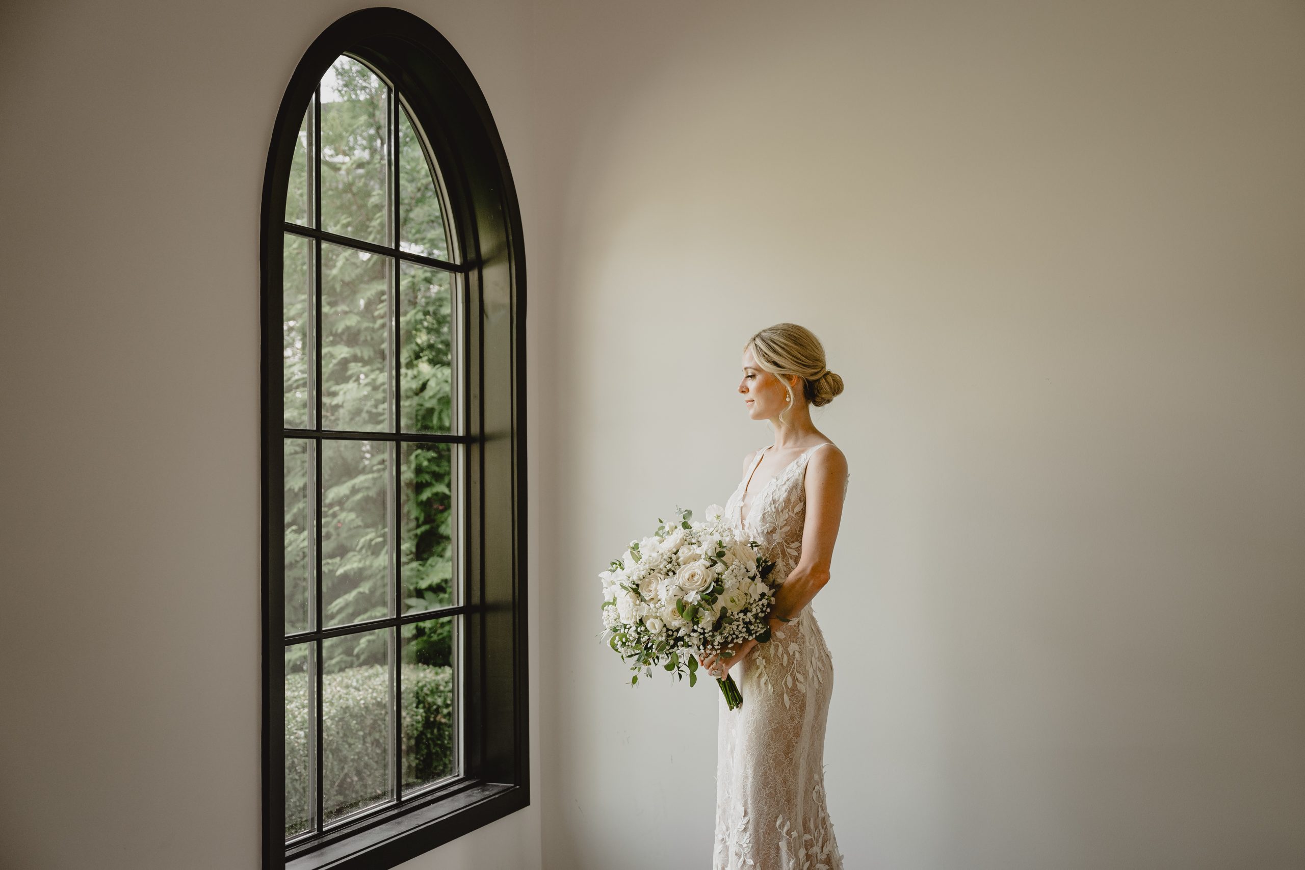 bride holds large bouquet of white roses and baby's breath by window at the Perona Farms Refinery