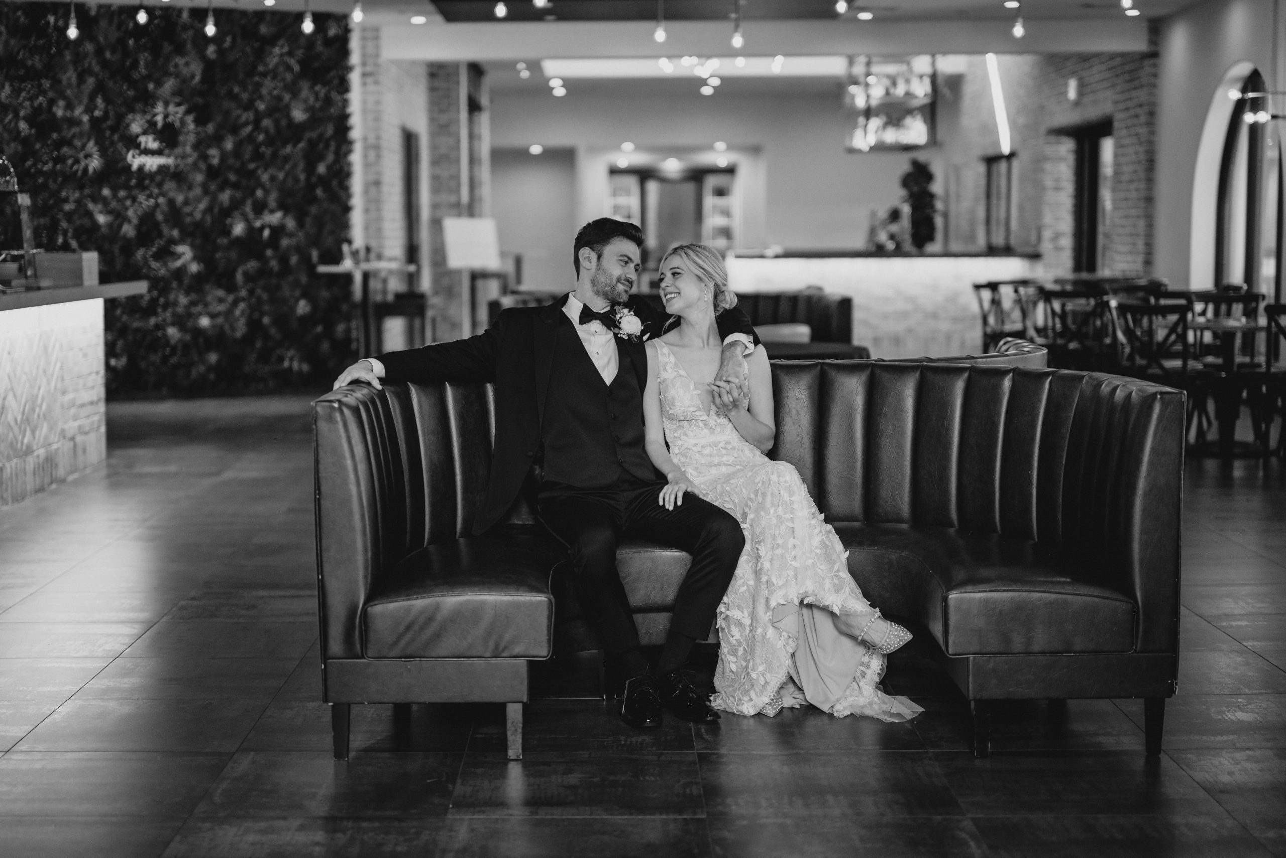 bride and groom sit together on U-shaped leather couch inside the Perona Farms Refinery