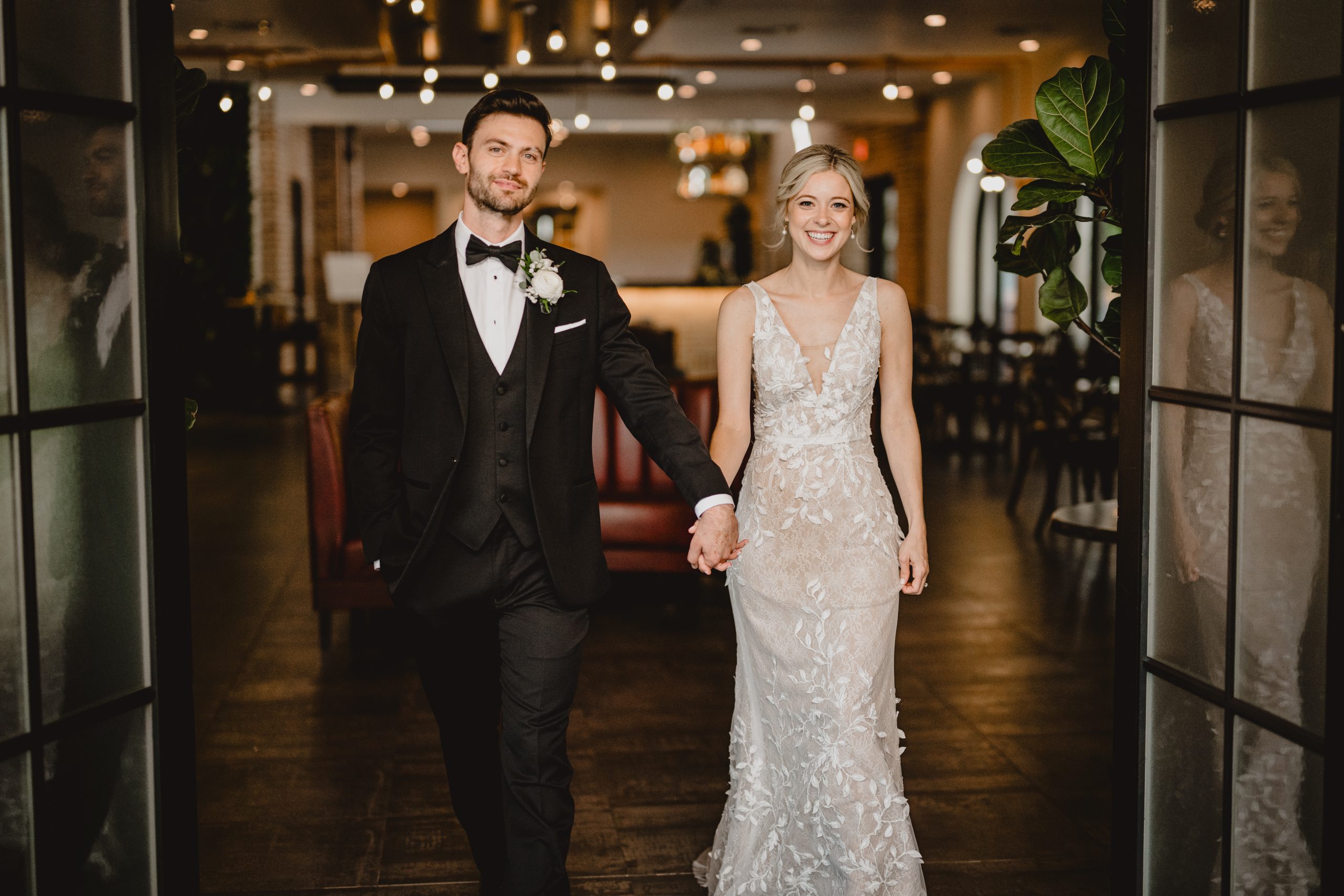 bride and groom hold hands walking through open doors at the Perona Farms Refinery