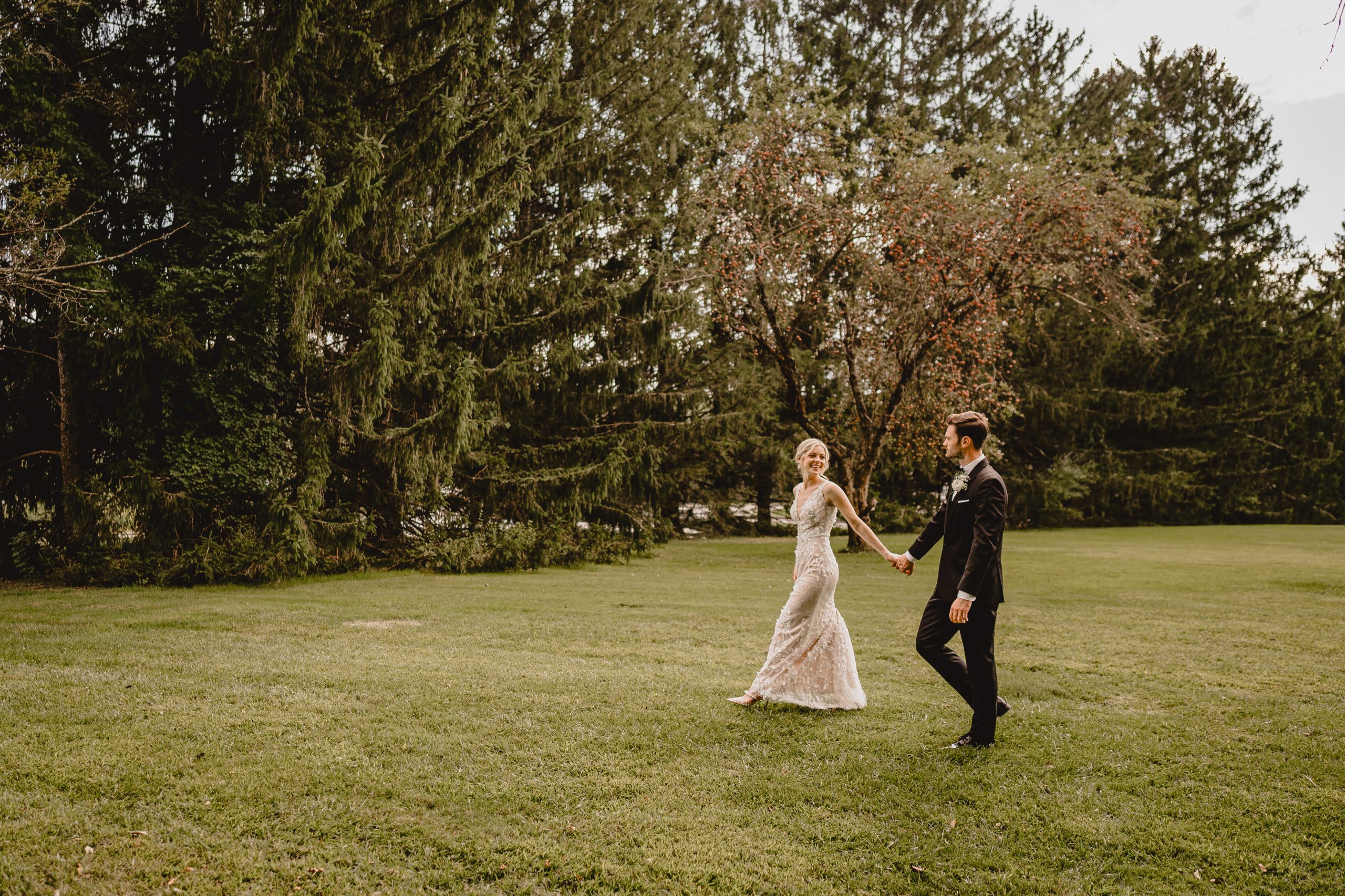 bride holds hands with groom leading him across the lawn at the Perona Farms Refinery