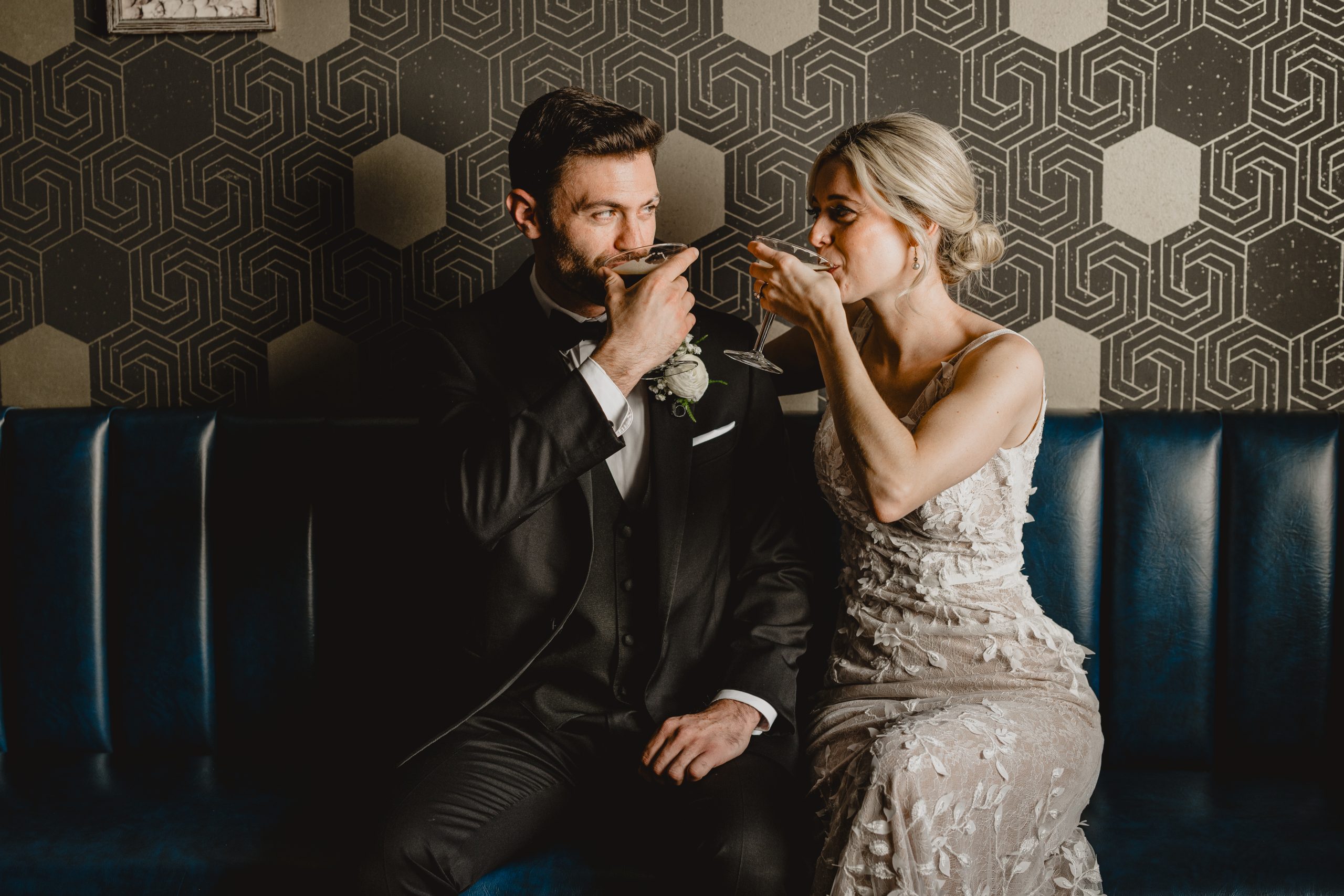 bride and groom drink espresso martinis looking at each other sitting on blue leather couch