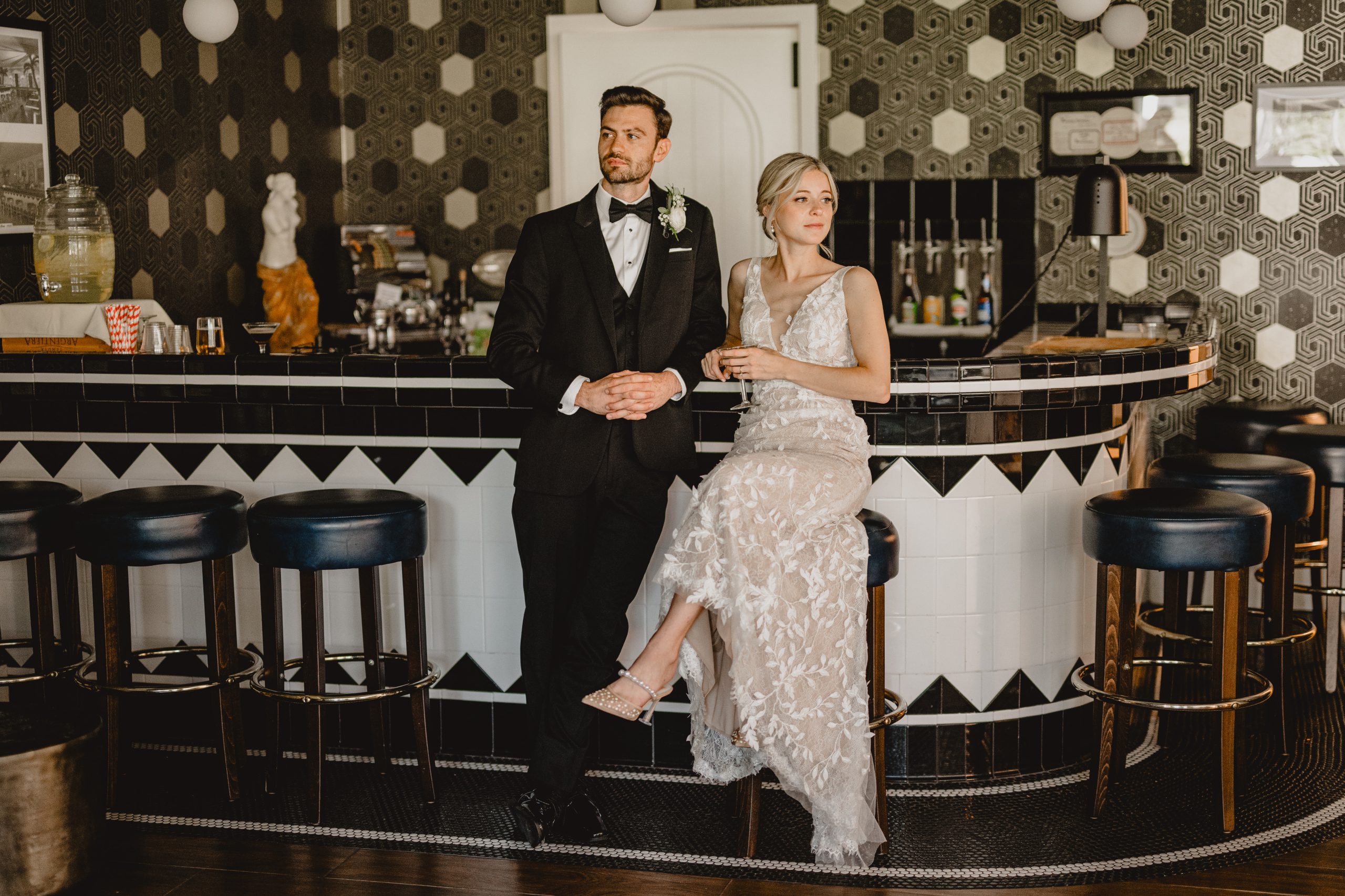 bride and groom lean against black and white tiled bar inside the Perona Farms Refinery