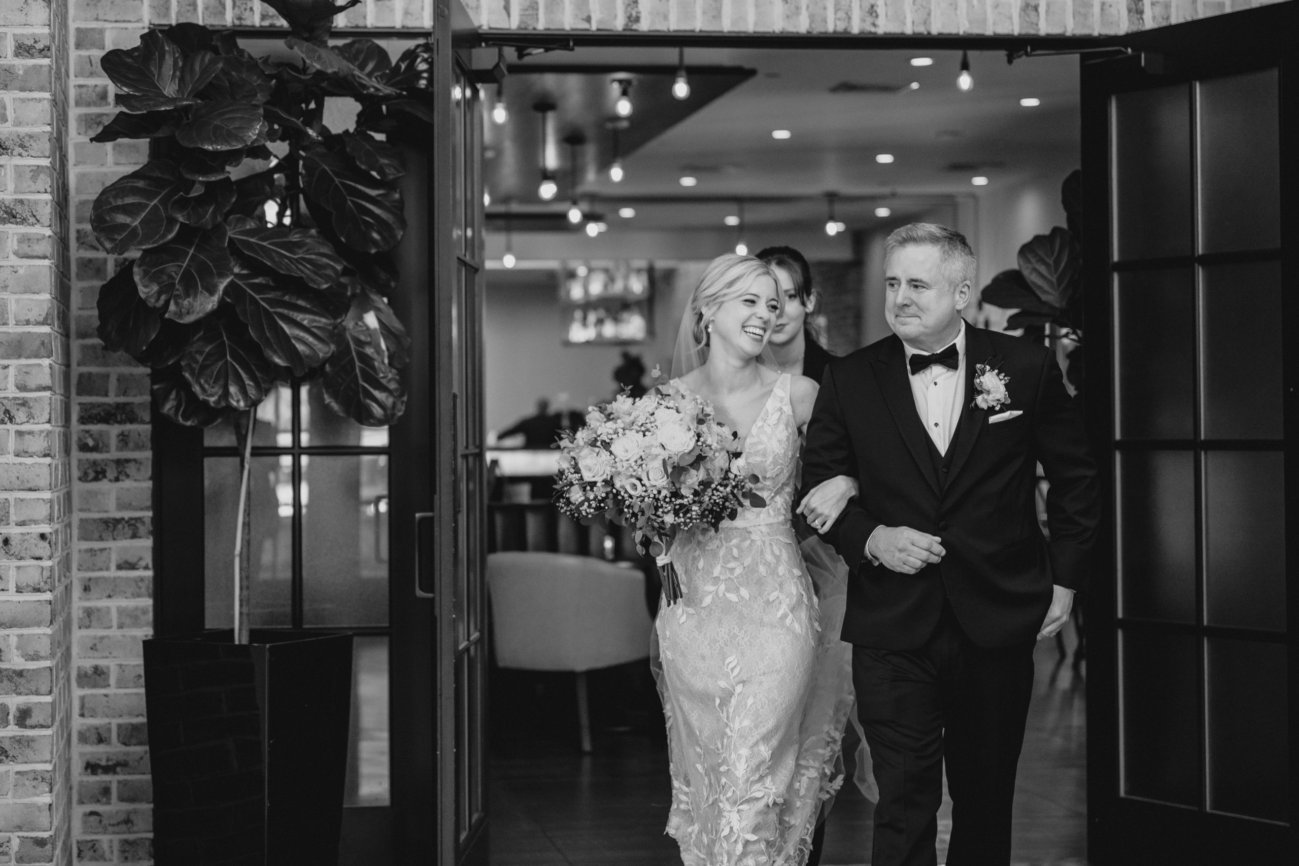 bride laughs walking on dad's arm out of doorway at the Perona Farms Refinery