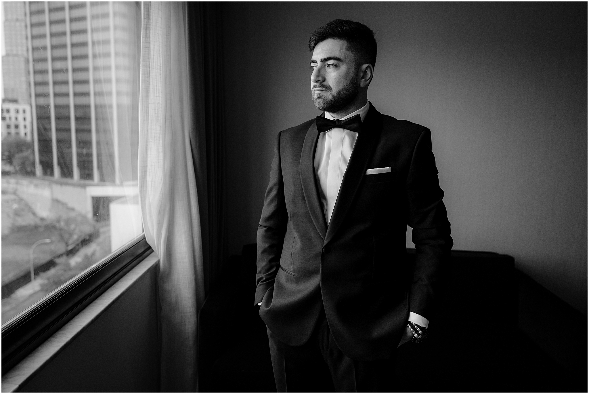 black and white photo of groom looking out the window of NYC hotel 