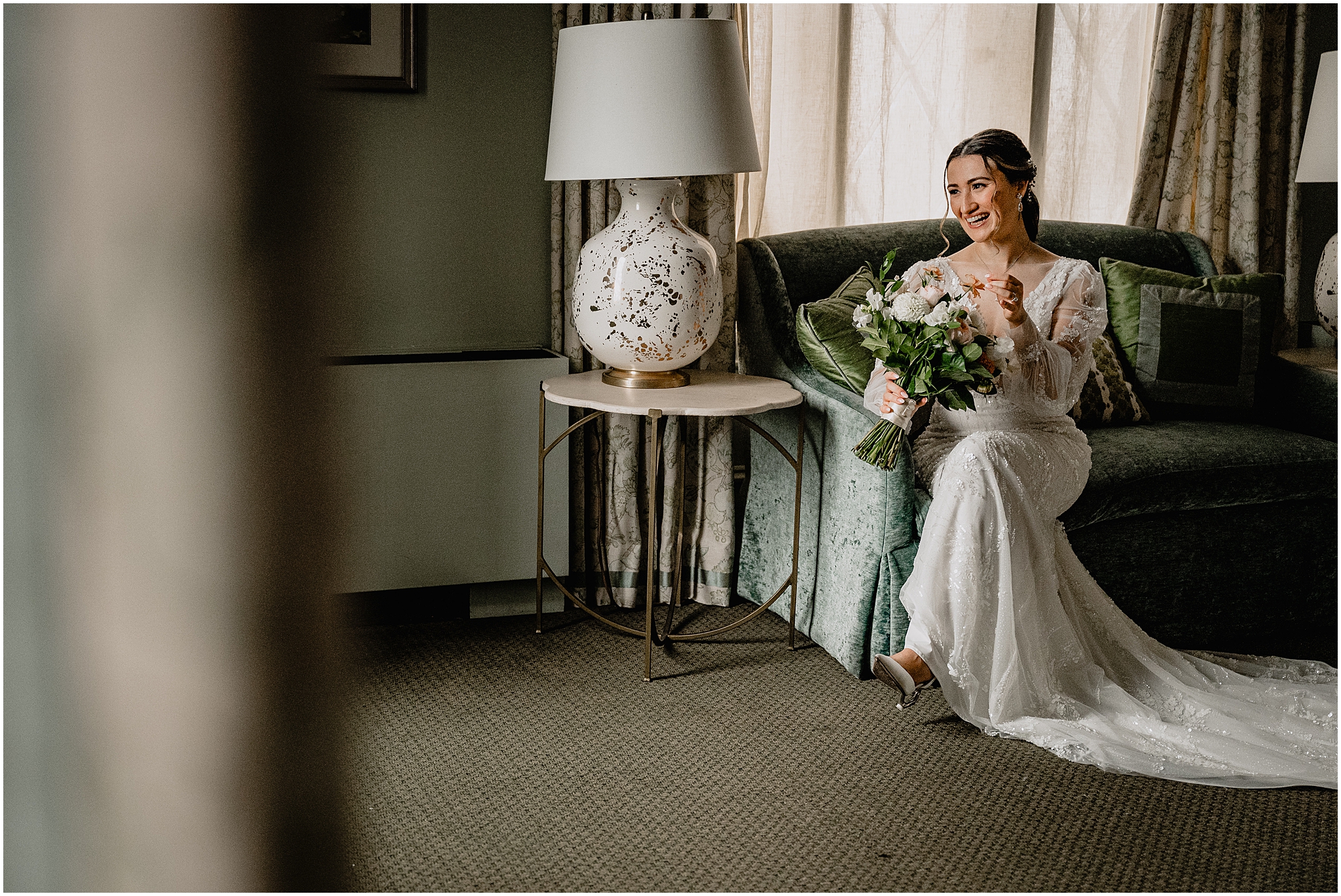 bride sits on green sofa in NYC Hotel room looking at bouquet of flowers 