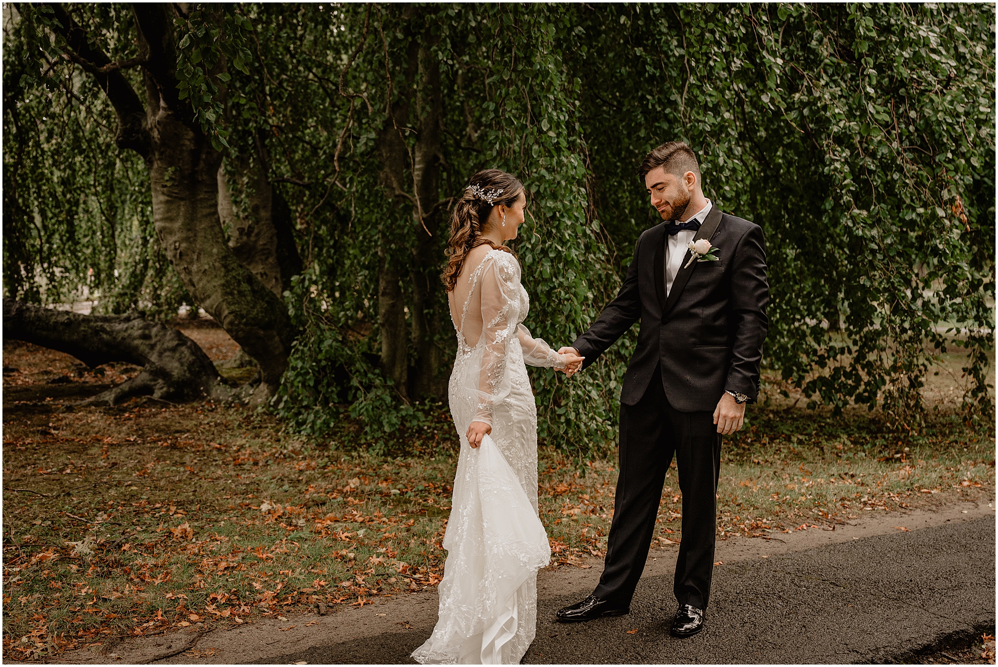 groom holds bride's hand looking at her during first look on driveway at Whitby Castle