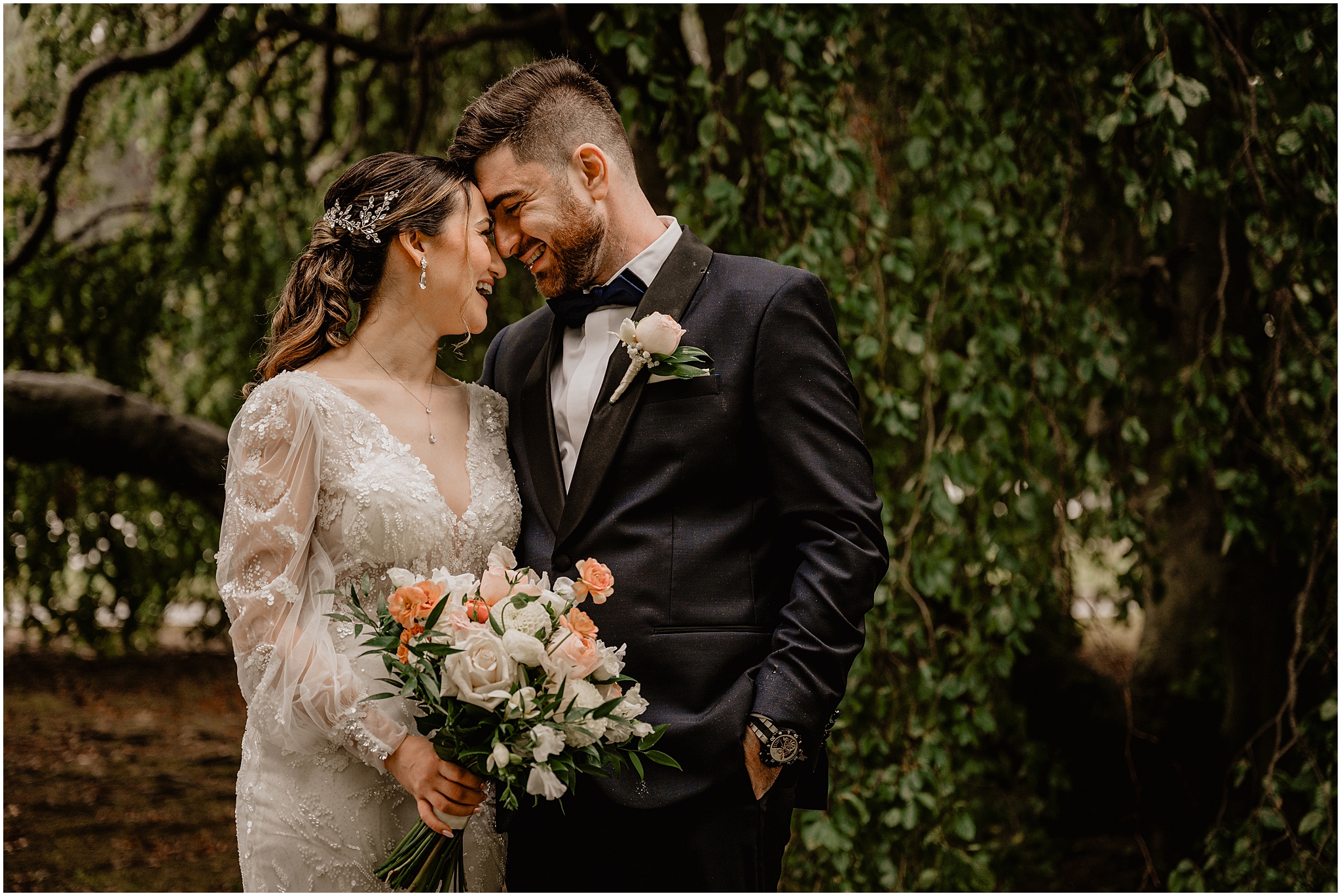 bride and groom smile leaning heads together while bird holds bouquet of coral and white flowers 