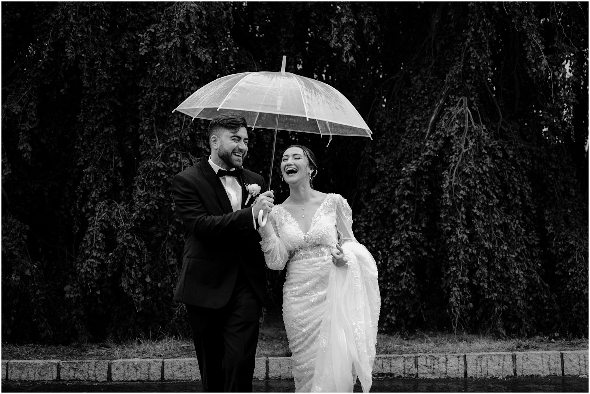 bride and groom laugh under clear umbrella in parking lot at Whitby Castle