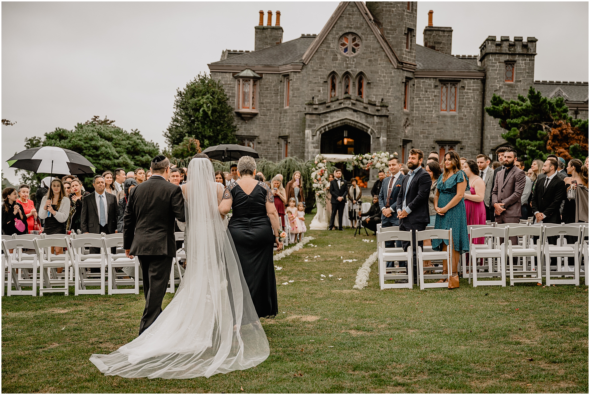 bride walks down aisle on lawn at Whitby Castle with parents 