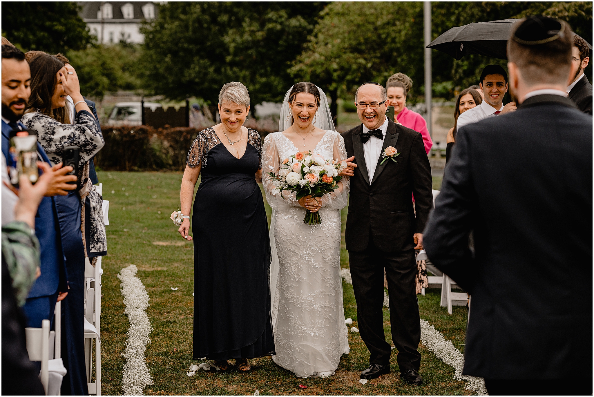 bride laughs at groom walking down aisle on lawn at Whitby Castle