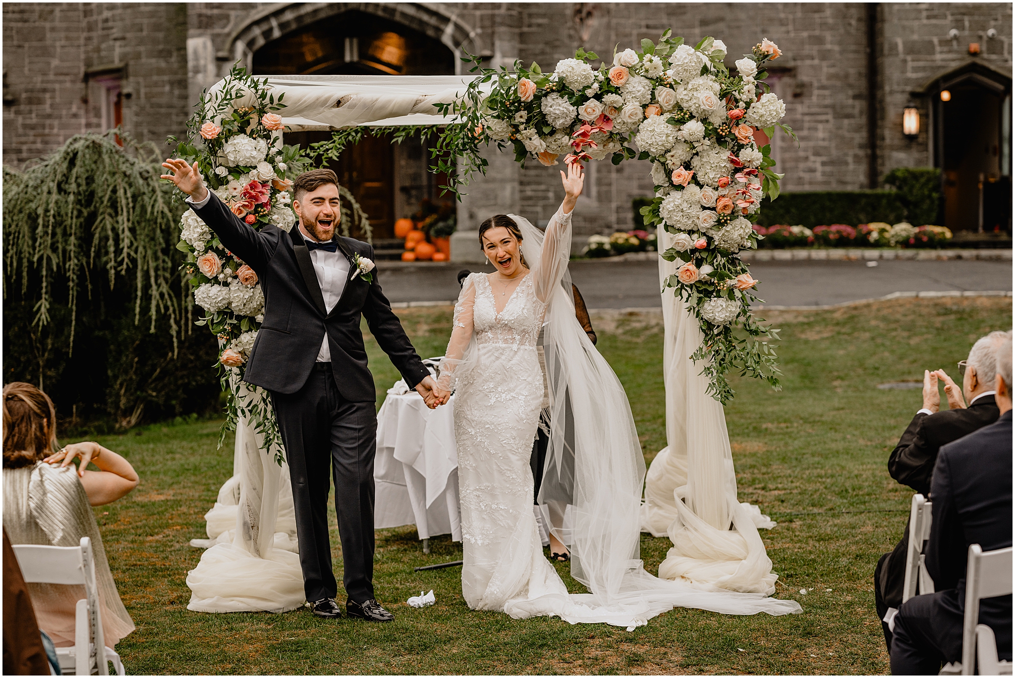 newlyweds cheer looking at guests on the lawn at Whitby Castle in front of chuppah 