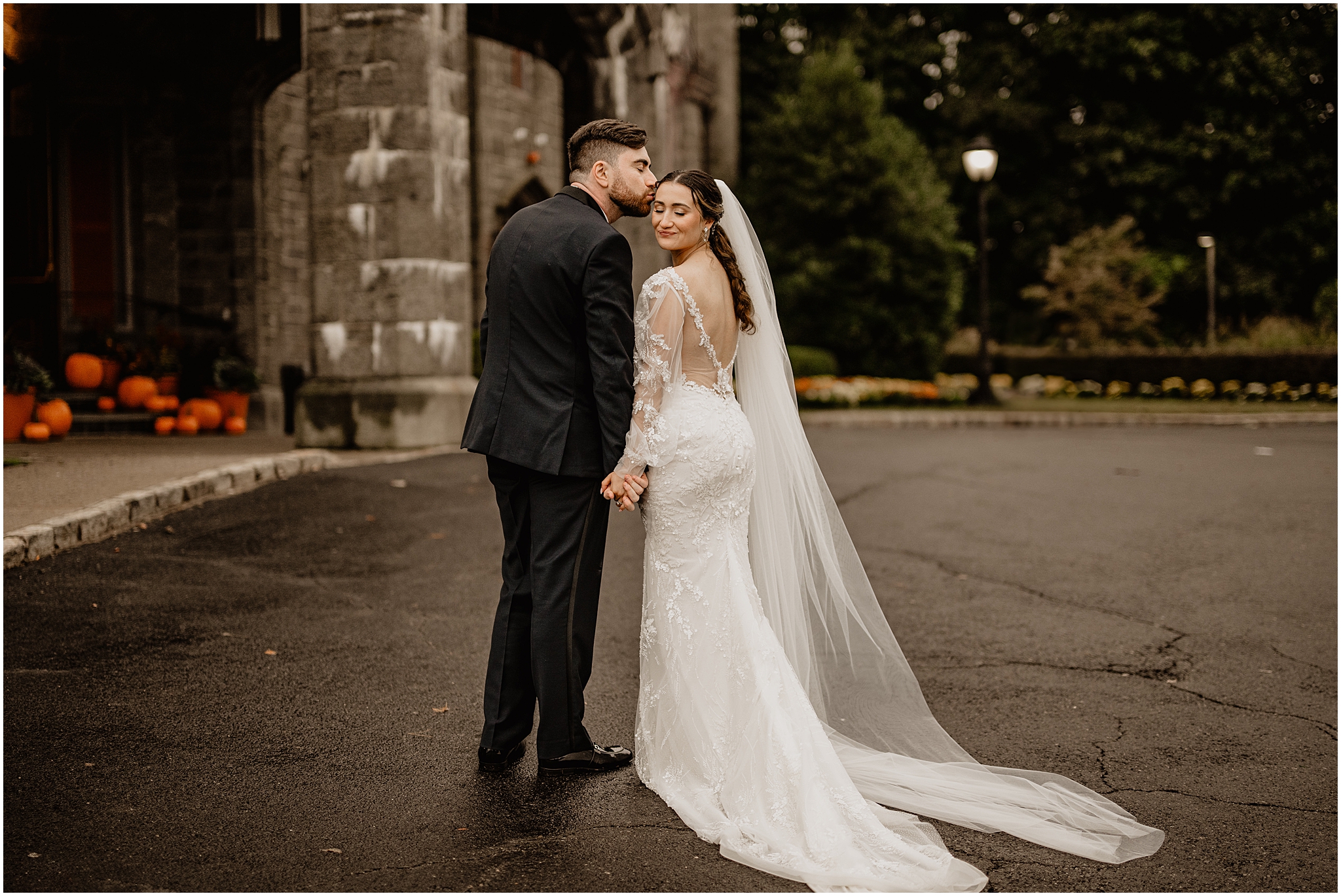 bride and groom hold hands while groom leans down to kiss bride's forehead outside Whitby Castle
