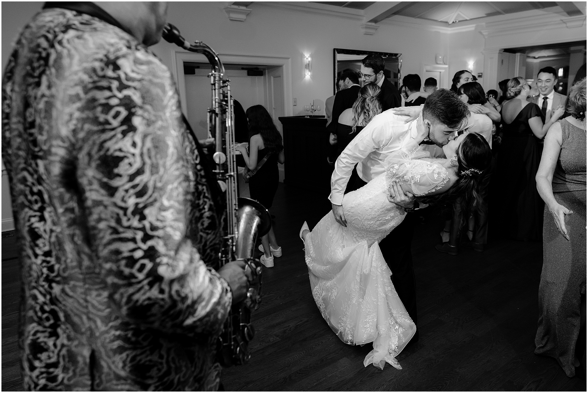 groom kisses bride dipping her near live musician playing saxophone at reception 