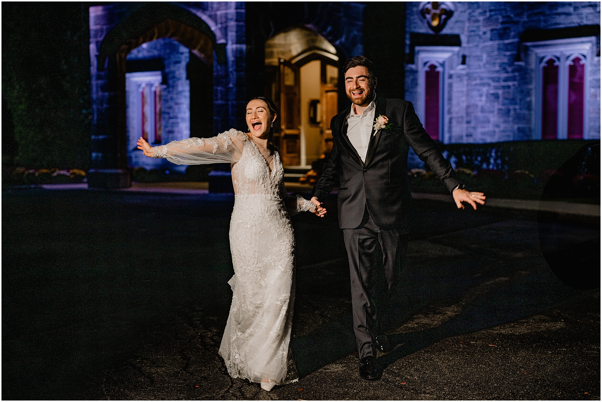 bride and groom walk outside Whitby Castle lit up blue at night 